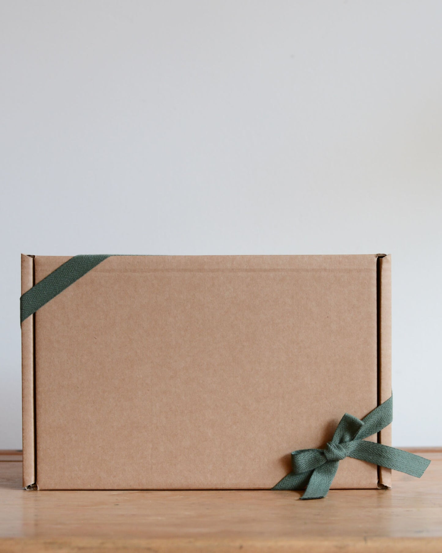 Cardboard gift box with a green ribbon on a wooden surface.