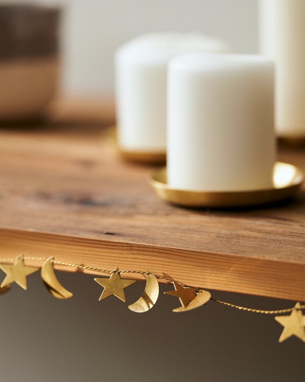 Brass moon and star garland on a wooden surface with white candles in the background.