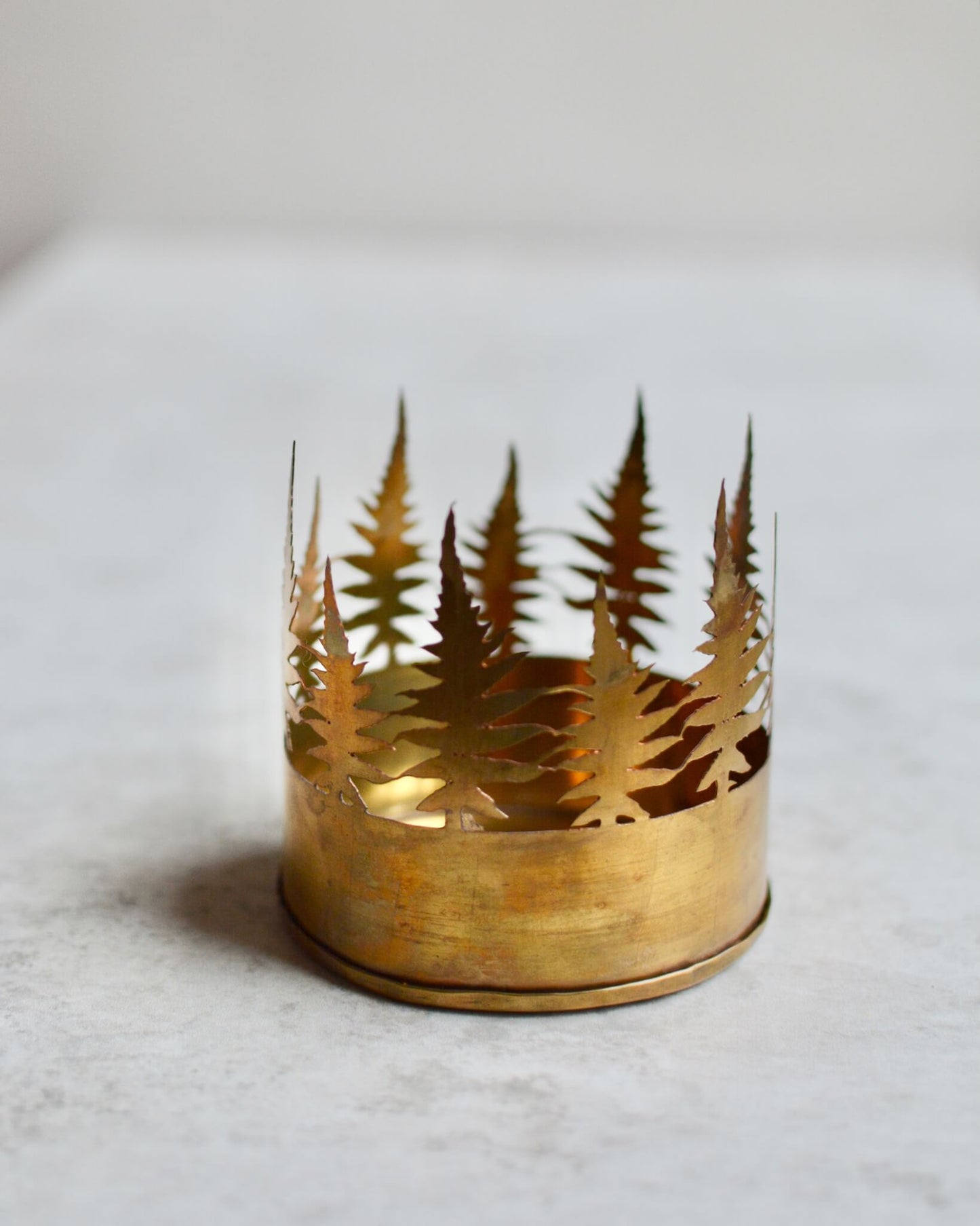 Gold candle holder with forest design on a light gray background.