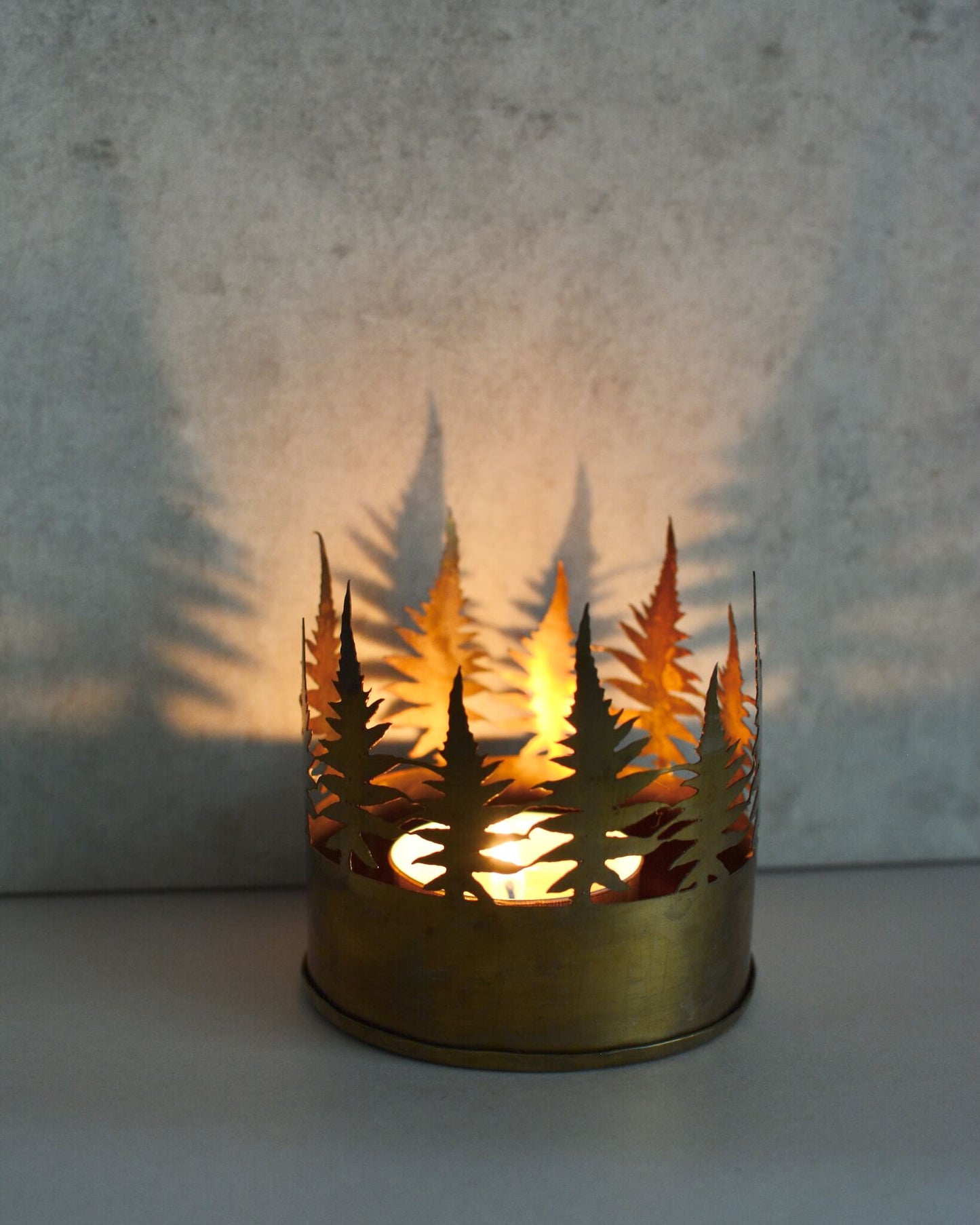 Decorative candle holder with leaf pattern casting a shadow on a wall.