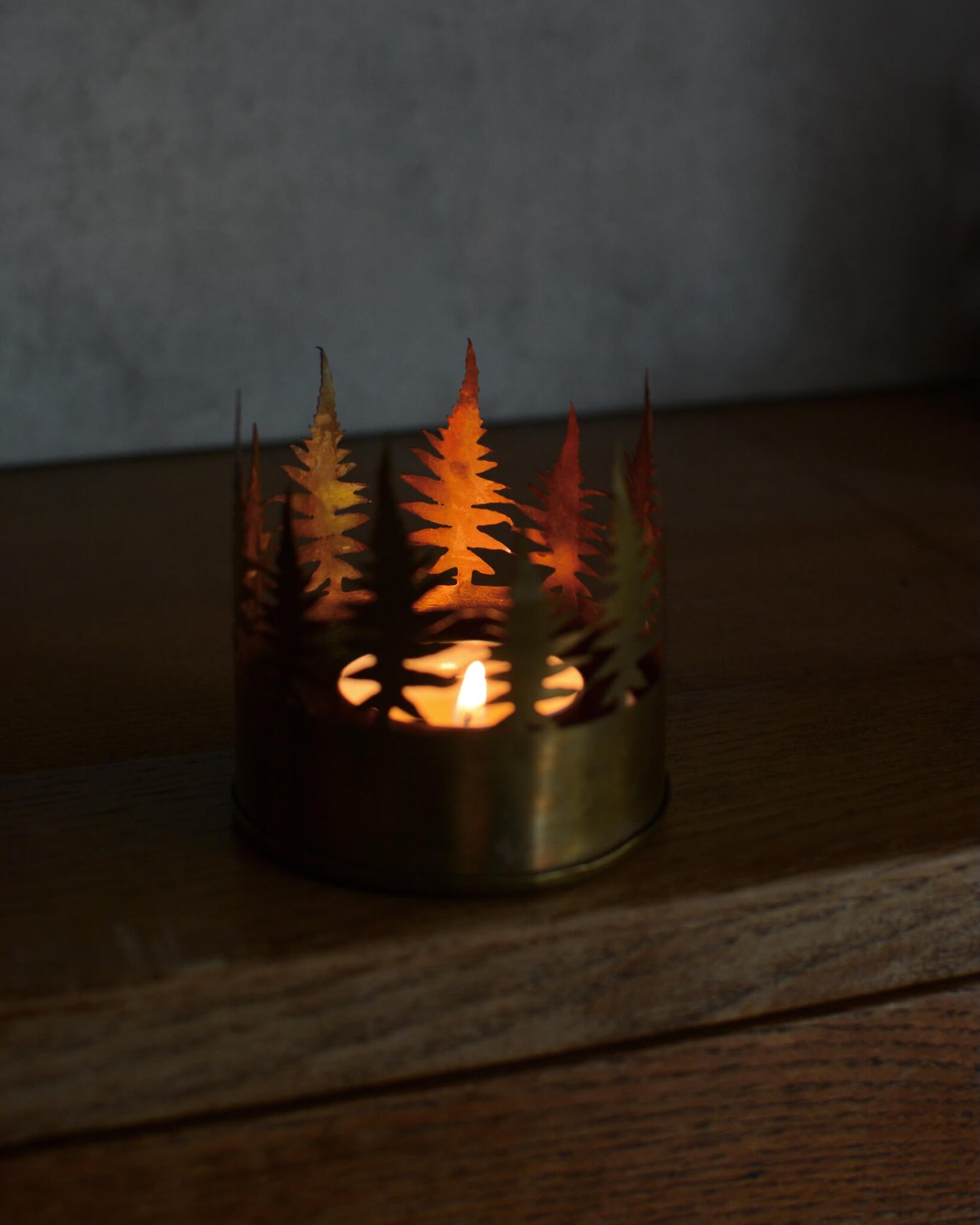 Candle holder with tree cutouts on a wooden surface.
