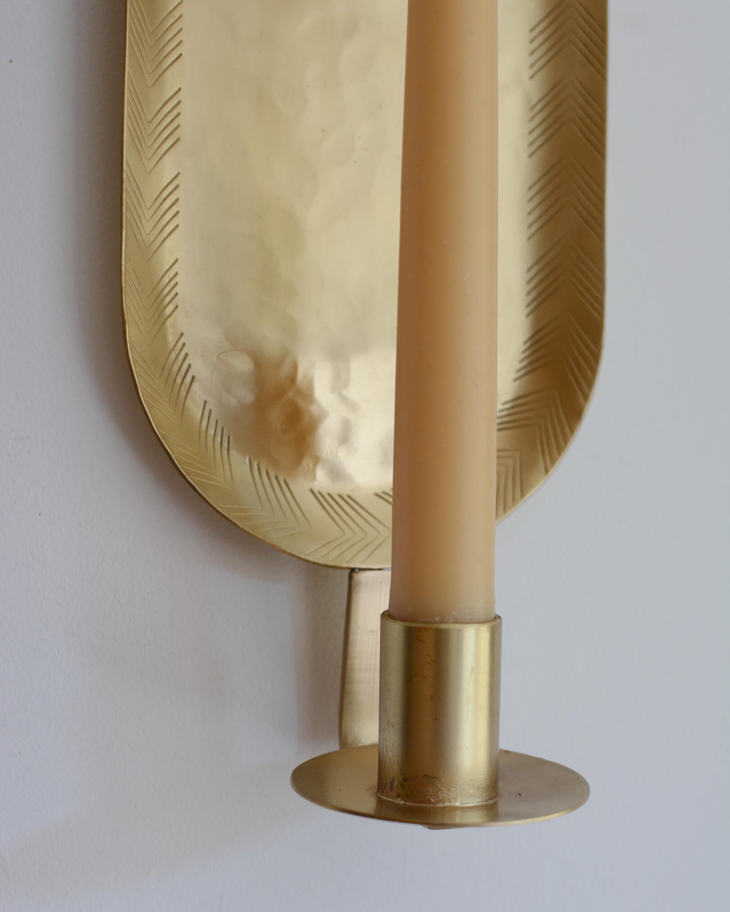 Detail of a brass candle wall sconce in an oval shape, with a lit beeswax taper candle.