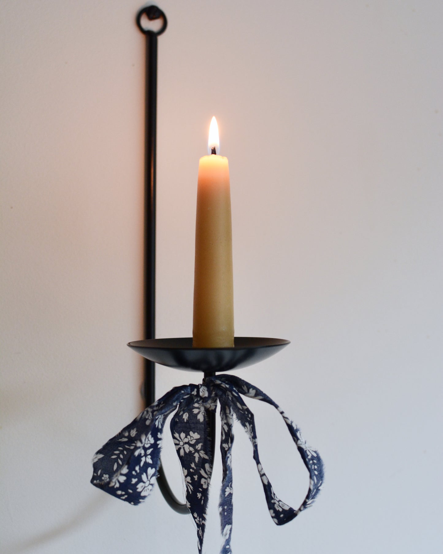 A beeswax dinner candle, on a black wall sconce, with a fabric bow beneath.