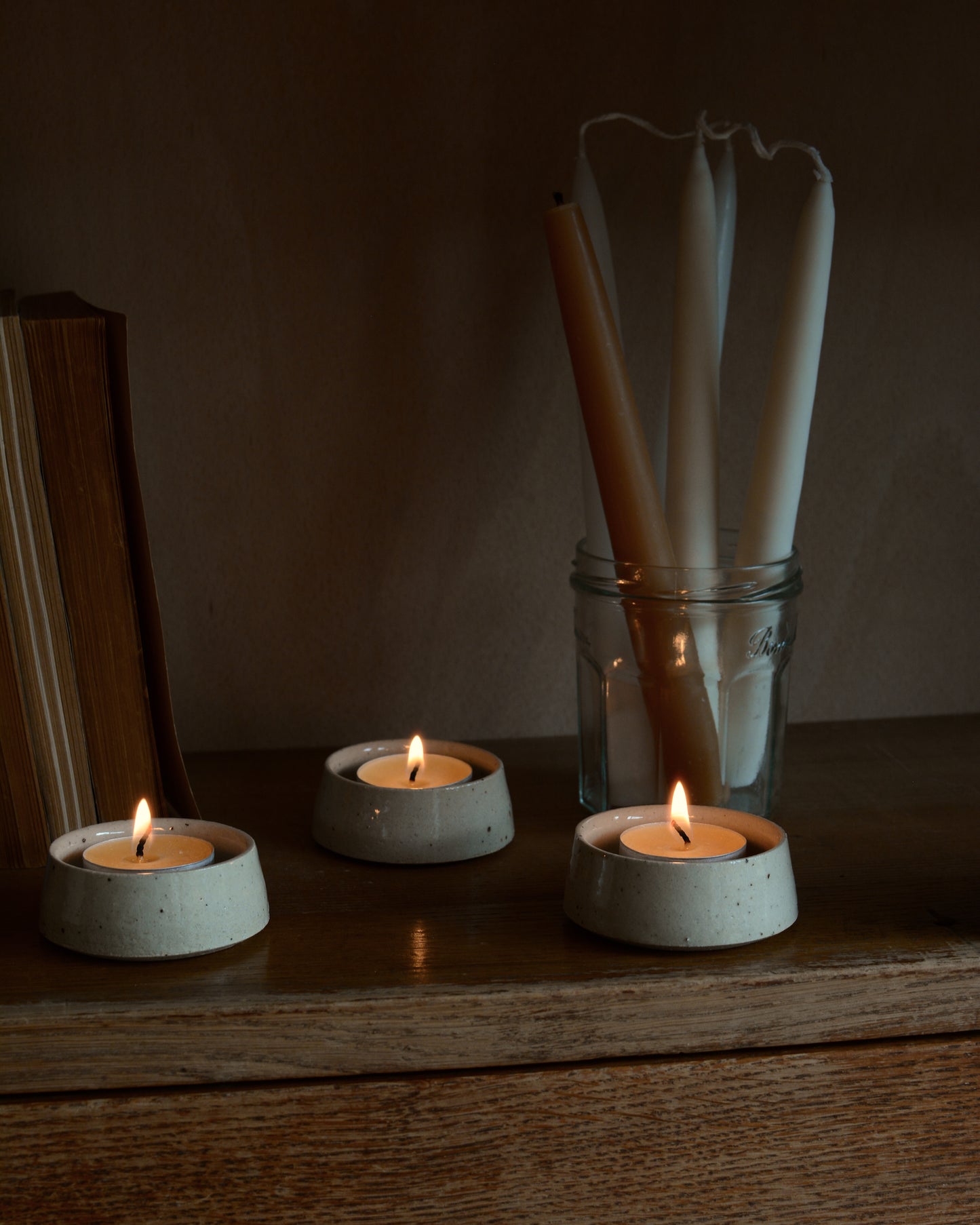 Beeswax dinner candles in a jam jar, alongside beeswax tea lights in ceramic holders.