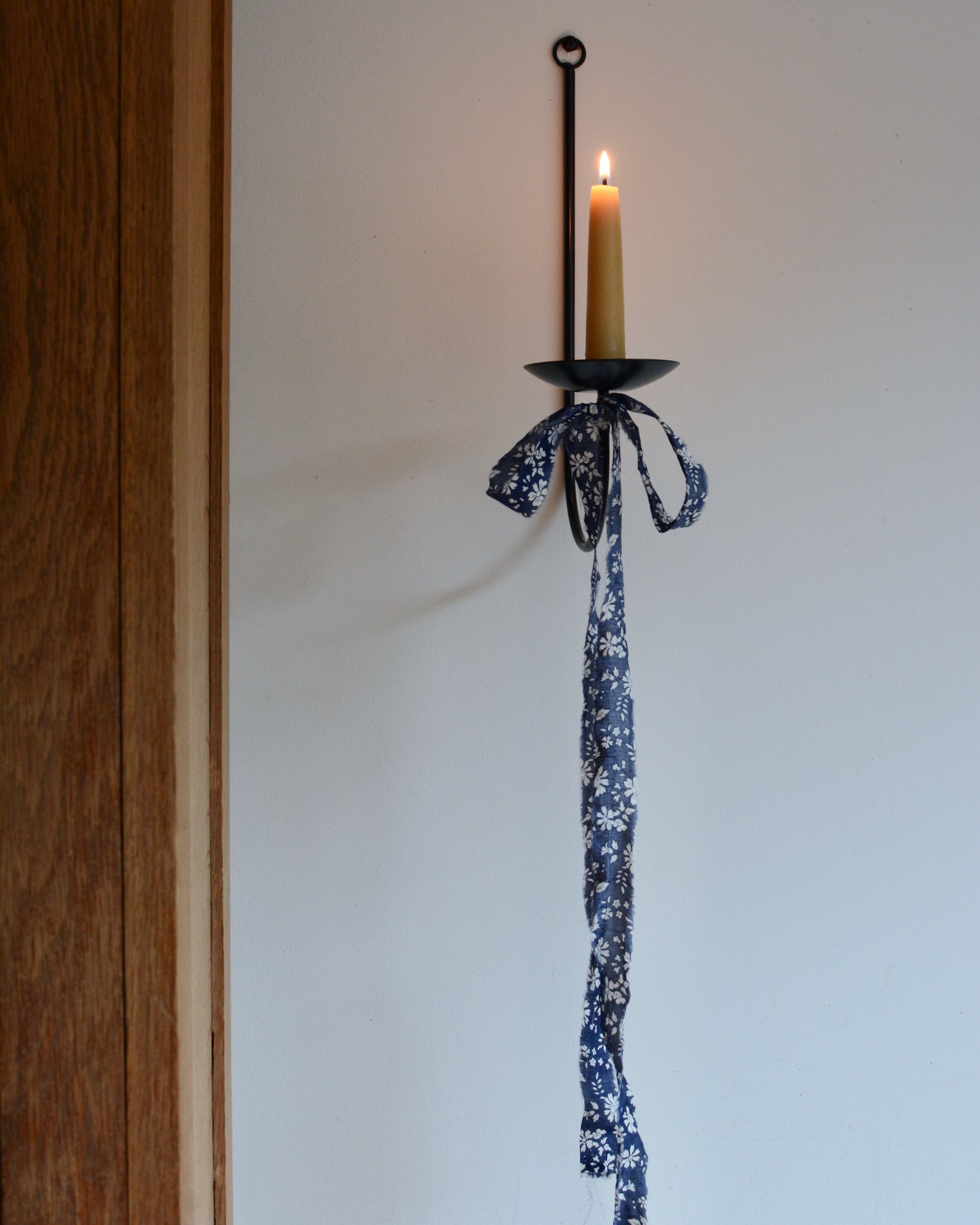 A pure beeswax short taper candle, in a black metal wall sconce, lit.