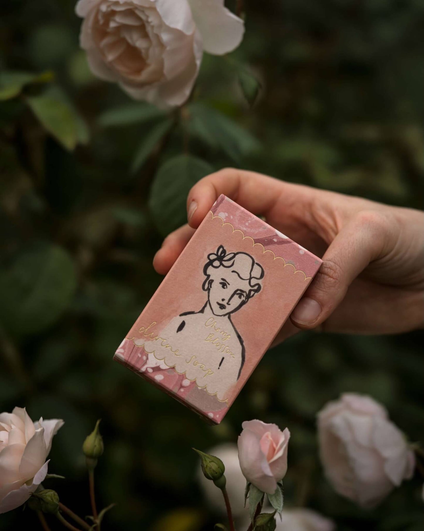 Hand holding a pink box of soap with a vintage-style illustration of a woman, surrounded by pink roses.