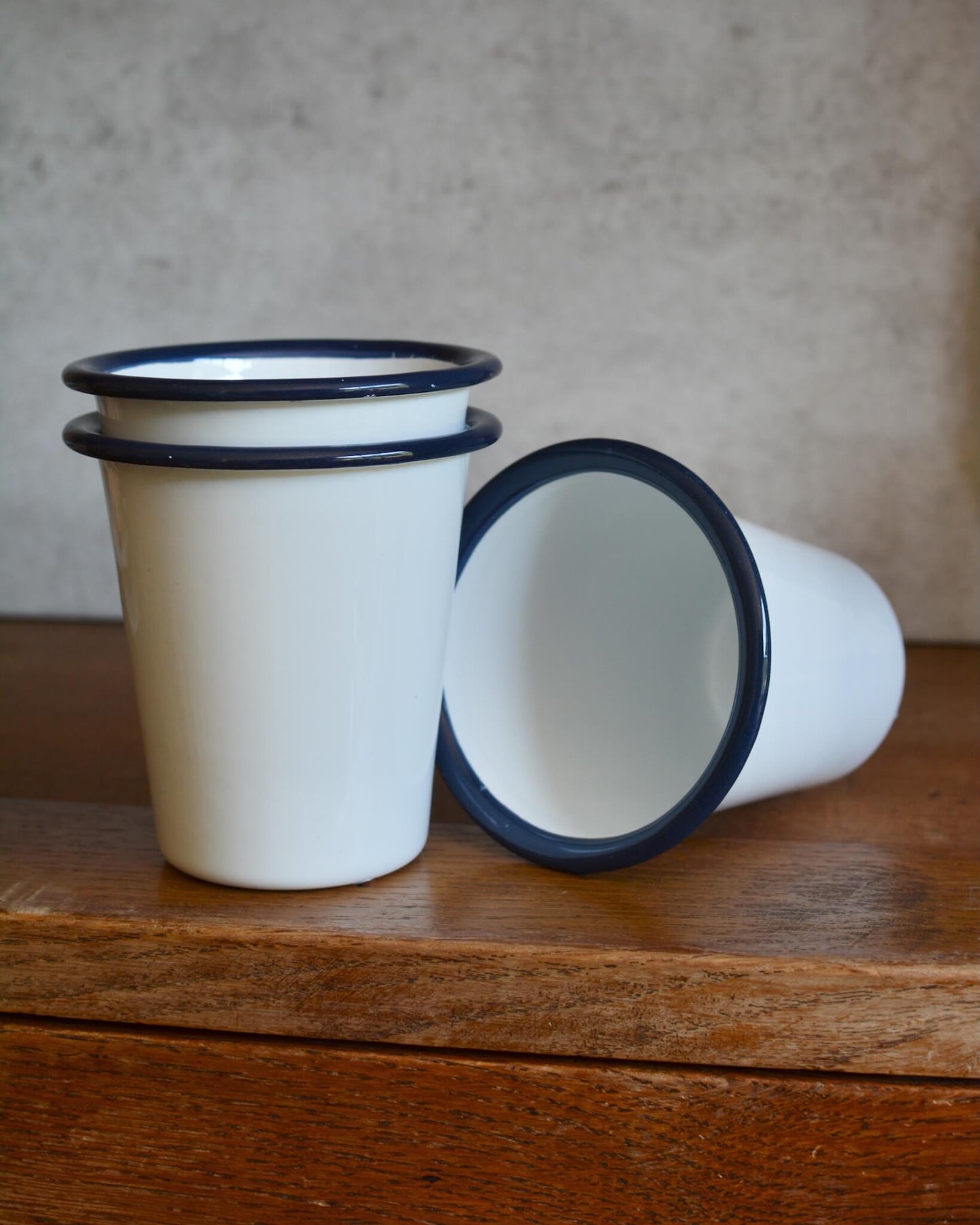 A stack of classic white enamel tumblers with navy rim.