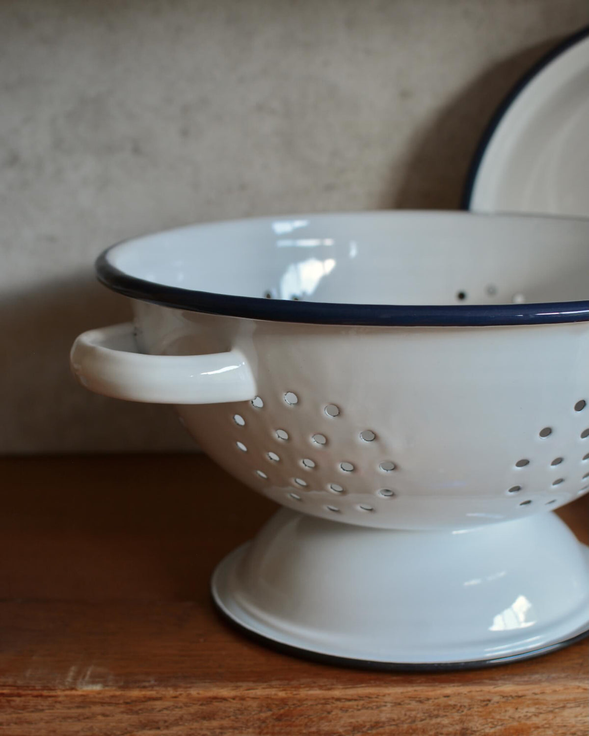 A classic white enamel kitchen colander with a navy blue rim.