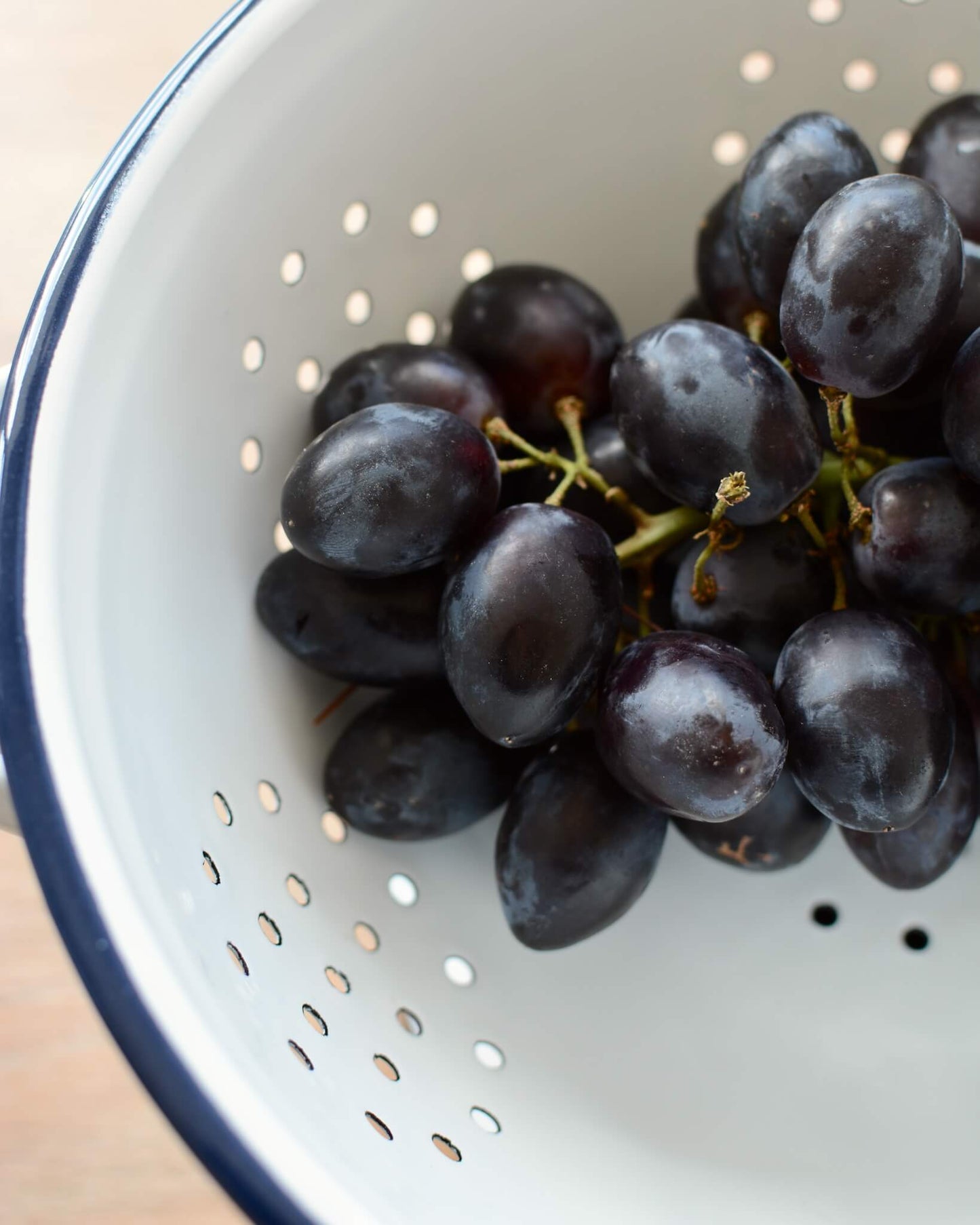 Detail shot of a classic white enamel kitchen colander with a navy blue rim and grapes within.