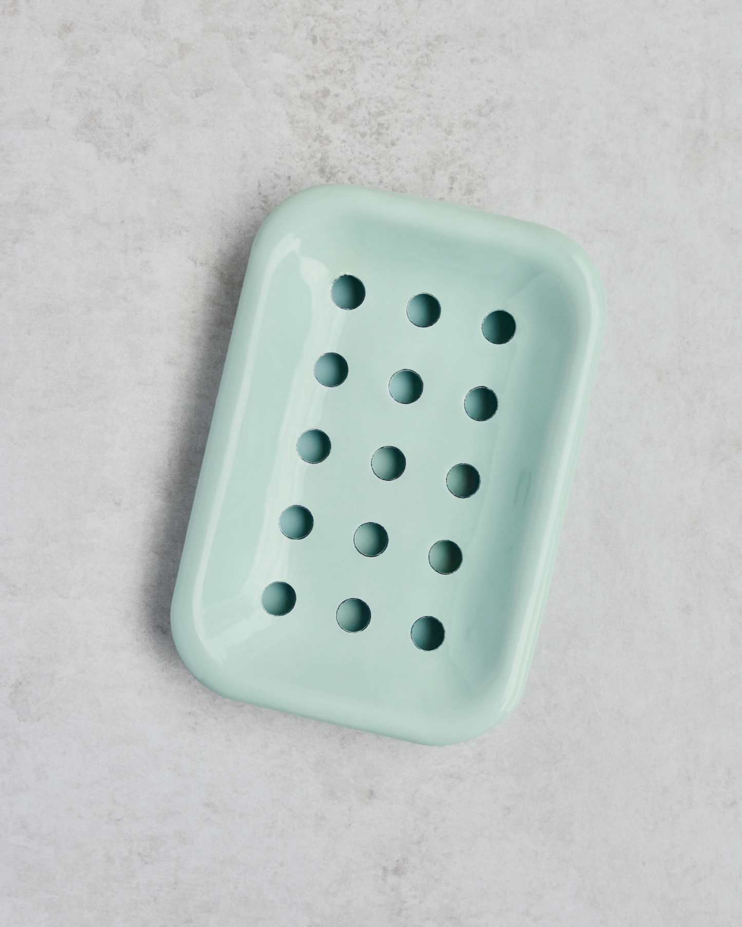 Pale mint green soap dish with holes on a grey surface.