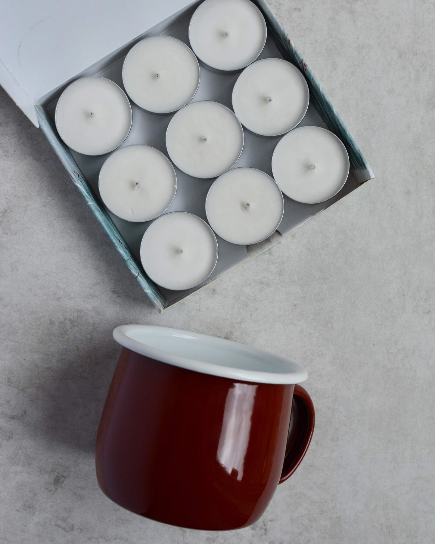 Box of white candles with a red mug on a gray surface
