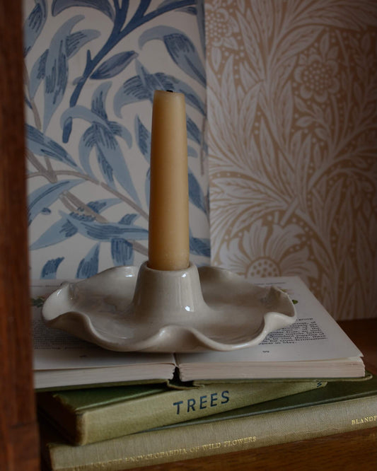 A ceramic candle holder with a frilly decorative edge, shown with a beeswax taper candle.