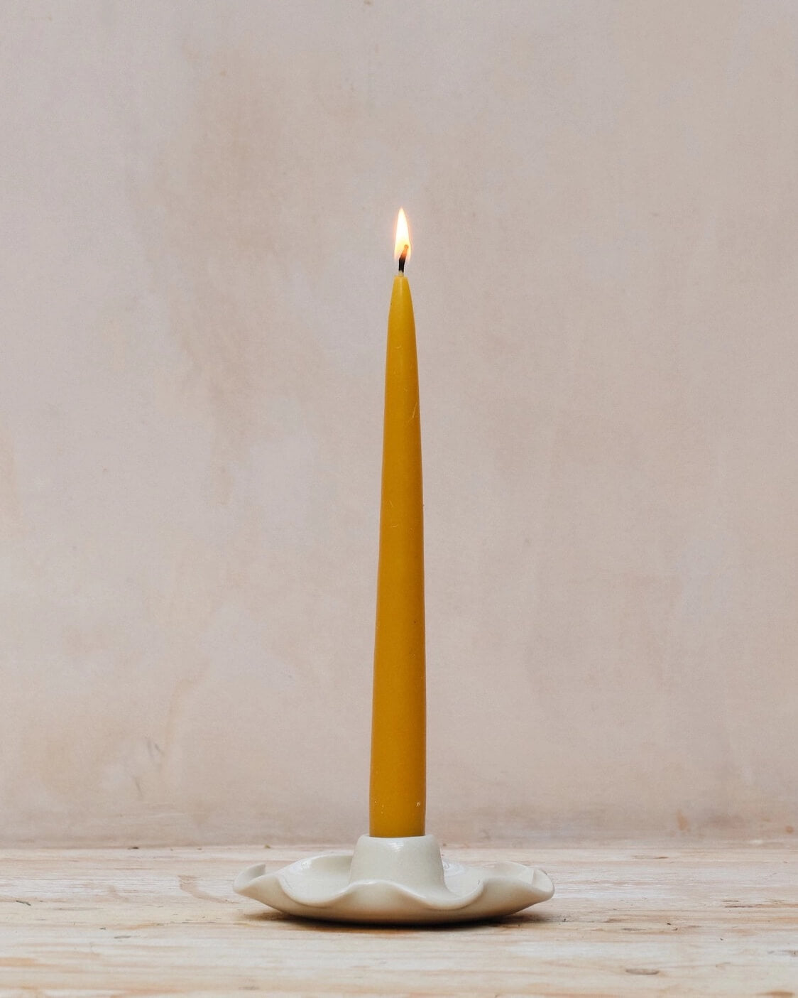 A ceramic candle holder with a frilly decorative edge, shown with a beeswax taper candle.