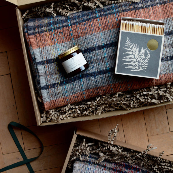 A gift box containing a recycled wool throw, jar candle and box of matches.
