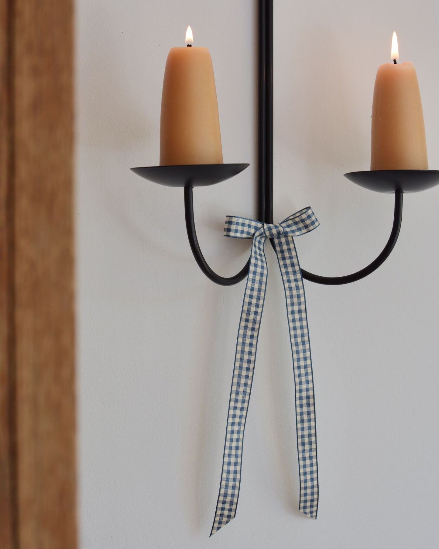A blue and white gingham bow, tied to a wall-mounted candle sconce.