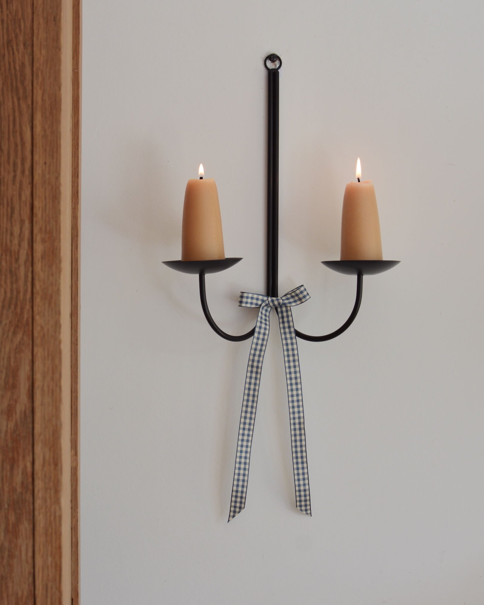 A blue and white gingham bow, tied to a wall-mounted candle sconce.