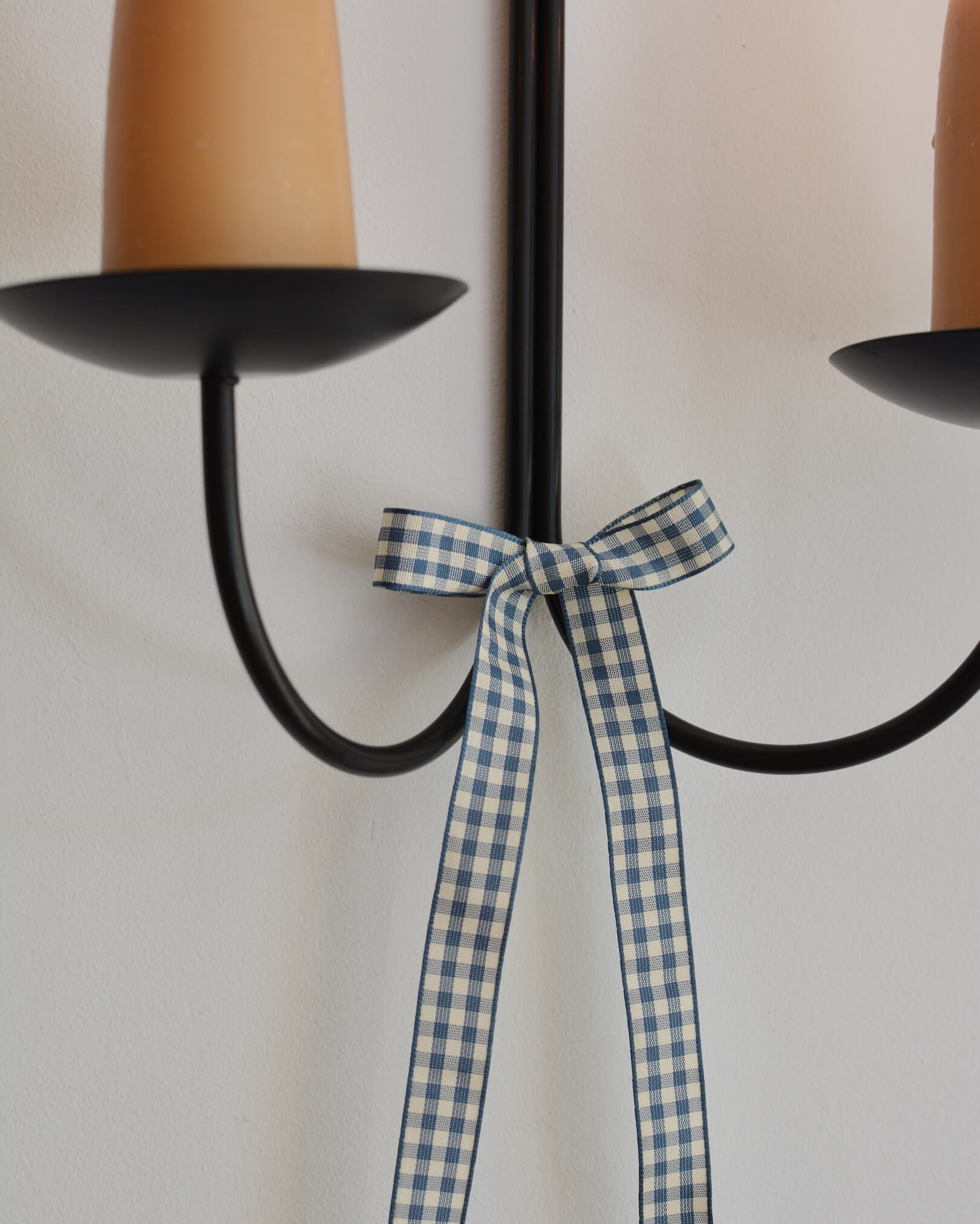 A blue and white gingham bow, tied to a wall-mounted candle sconce.
