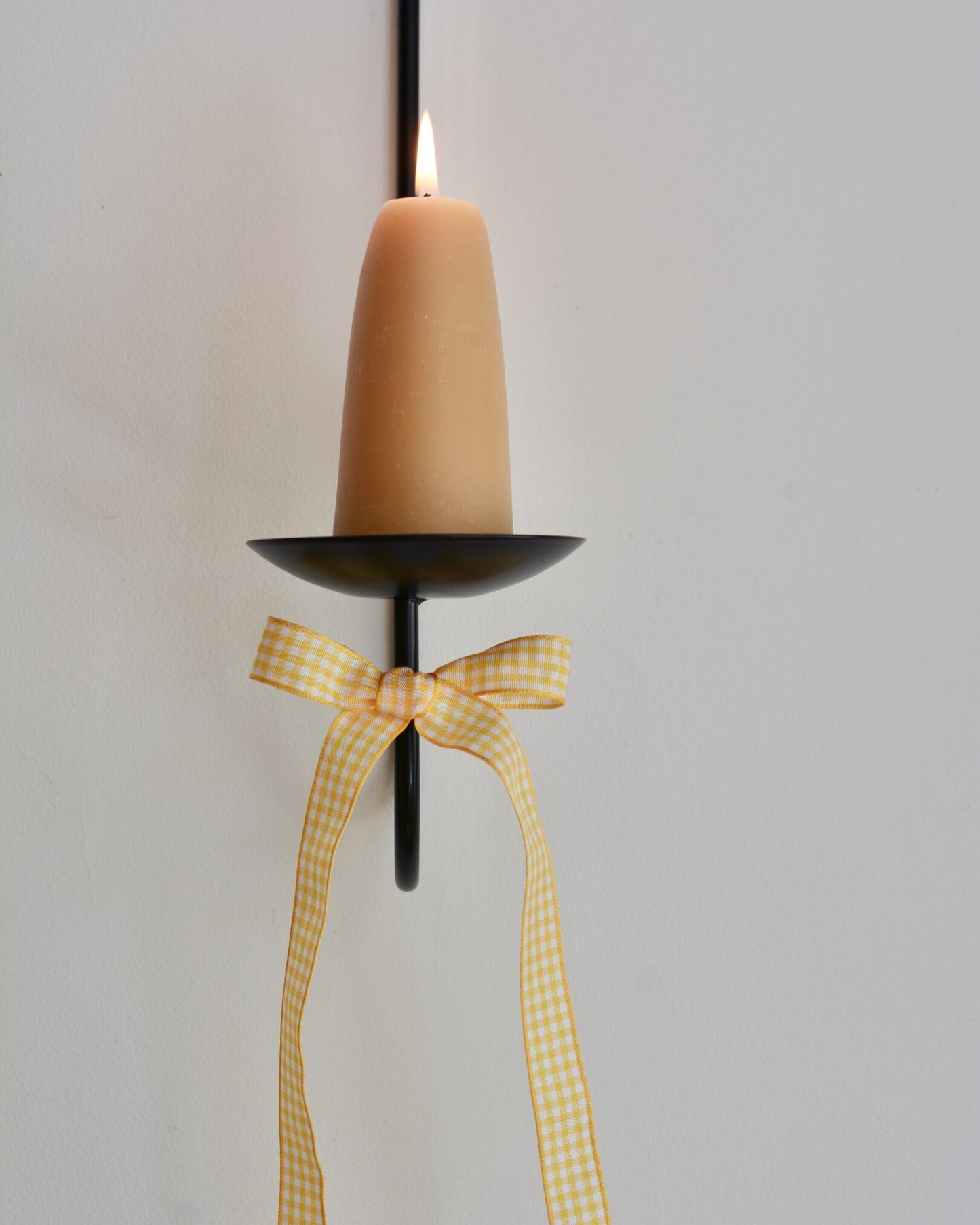 A yellow and white gingham bow, tied to a wall-mounted candle sconce.