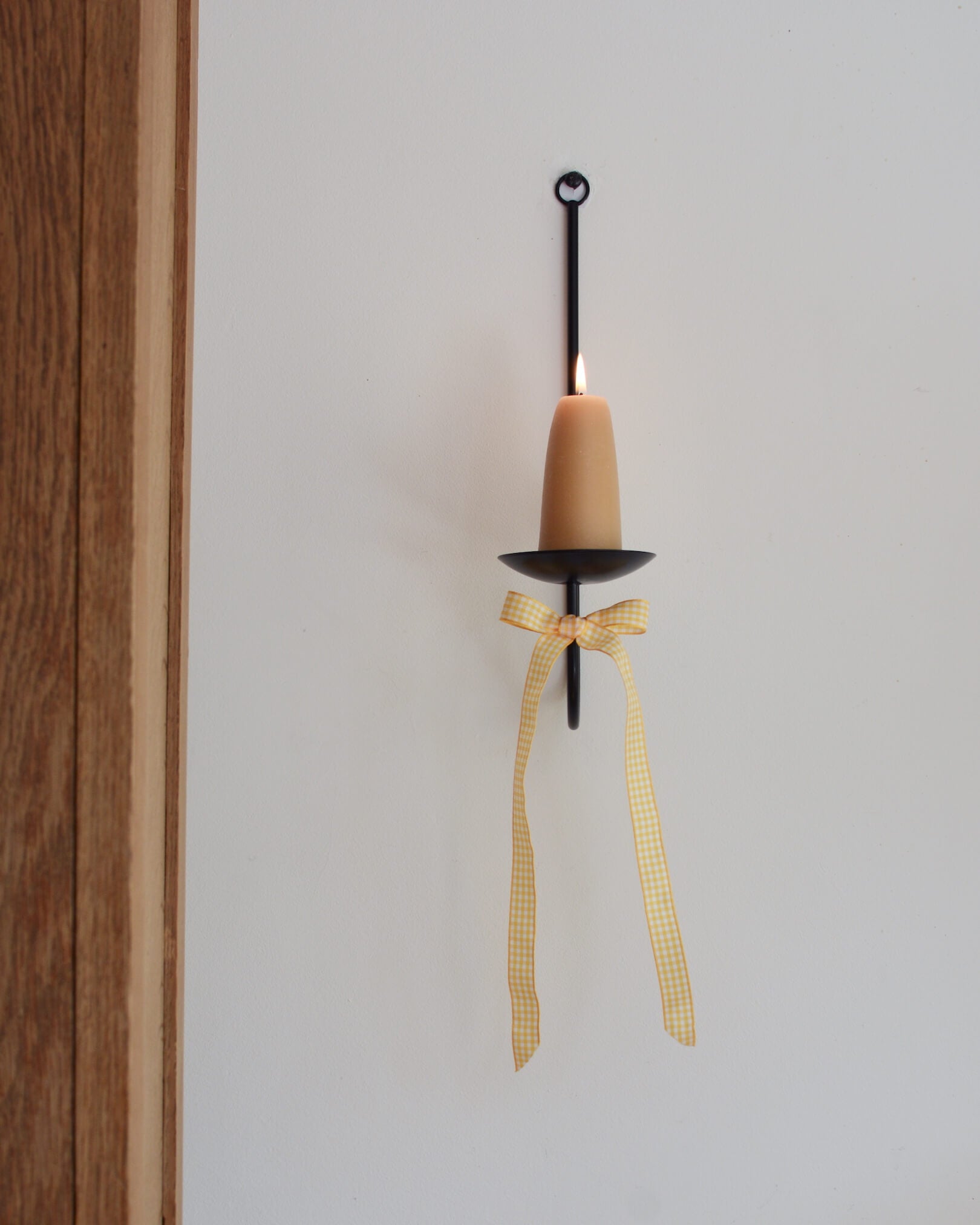 A yellow and white gingham bow, tied to a wall-mounted candle sconce.