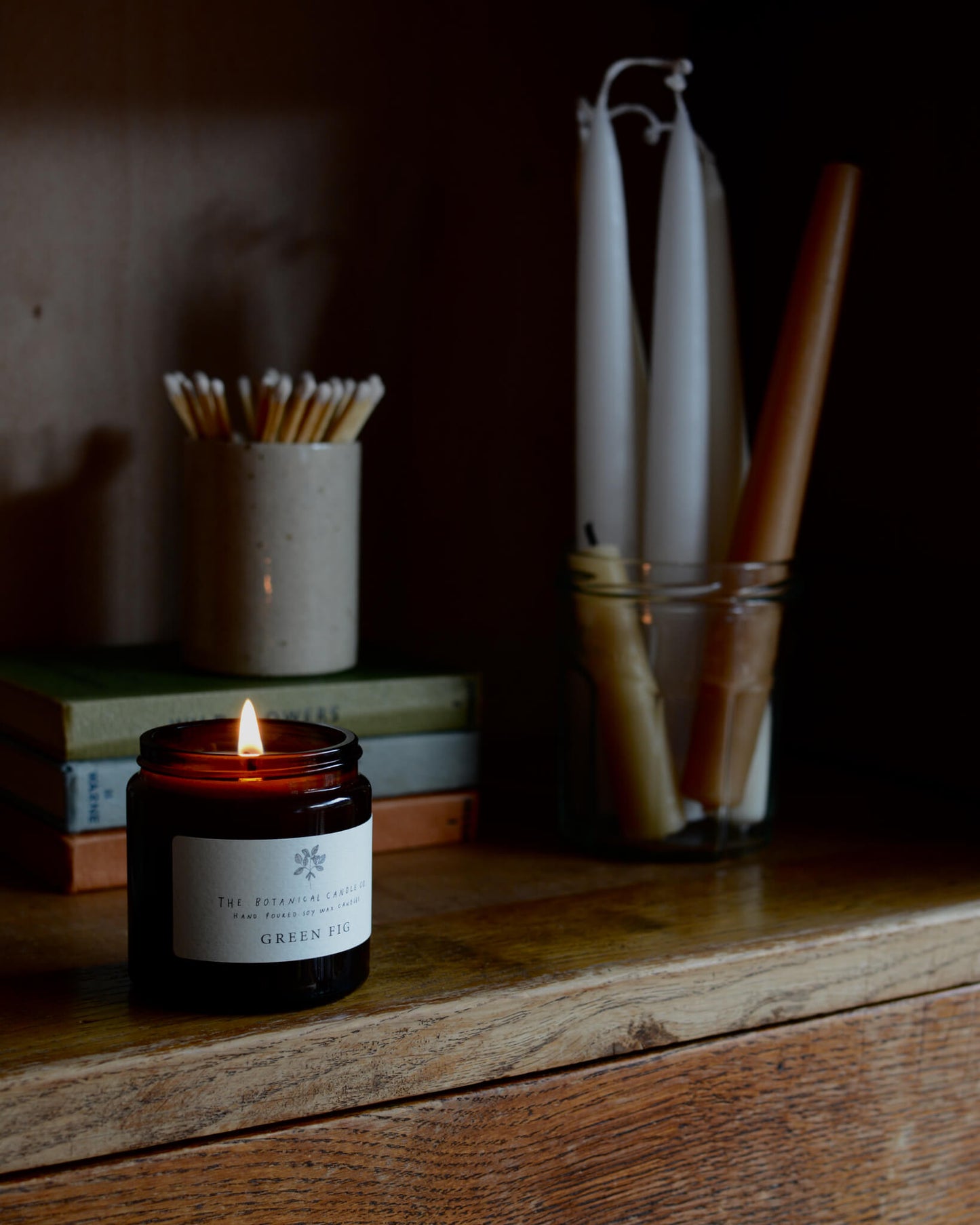Green fig scented soy candle by The Botanical Candle Co, on top of a wooden cabinet.