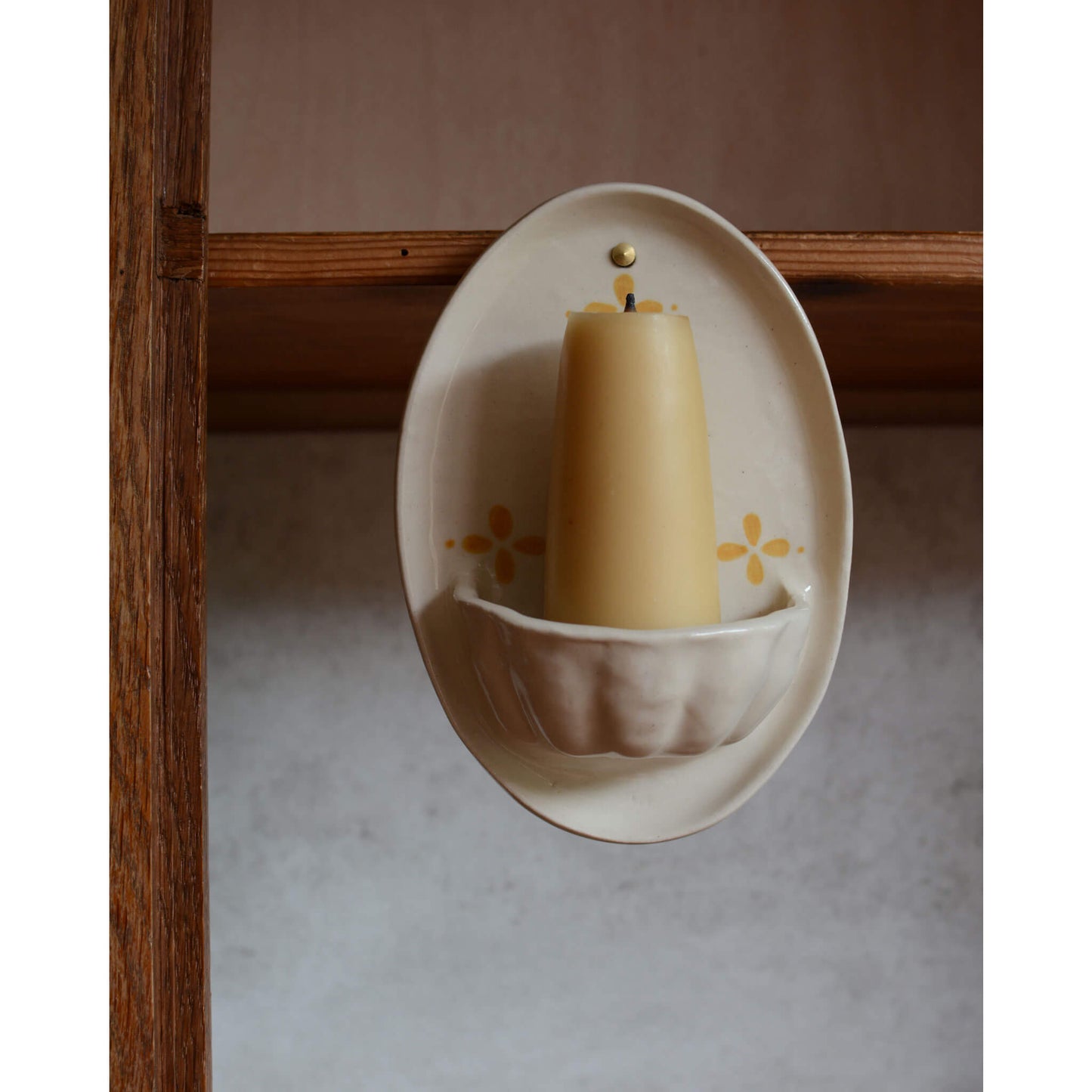 A close up of a cream and yellow ceramic candle wall sconce.