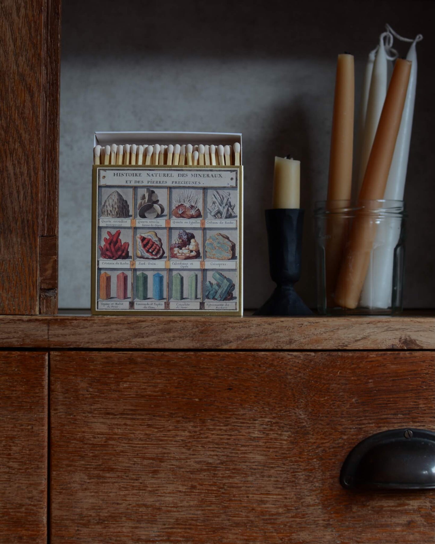 Match box with an illustration of minerals, alongside beeswax candles and candle holders.