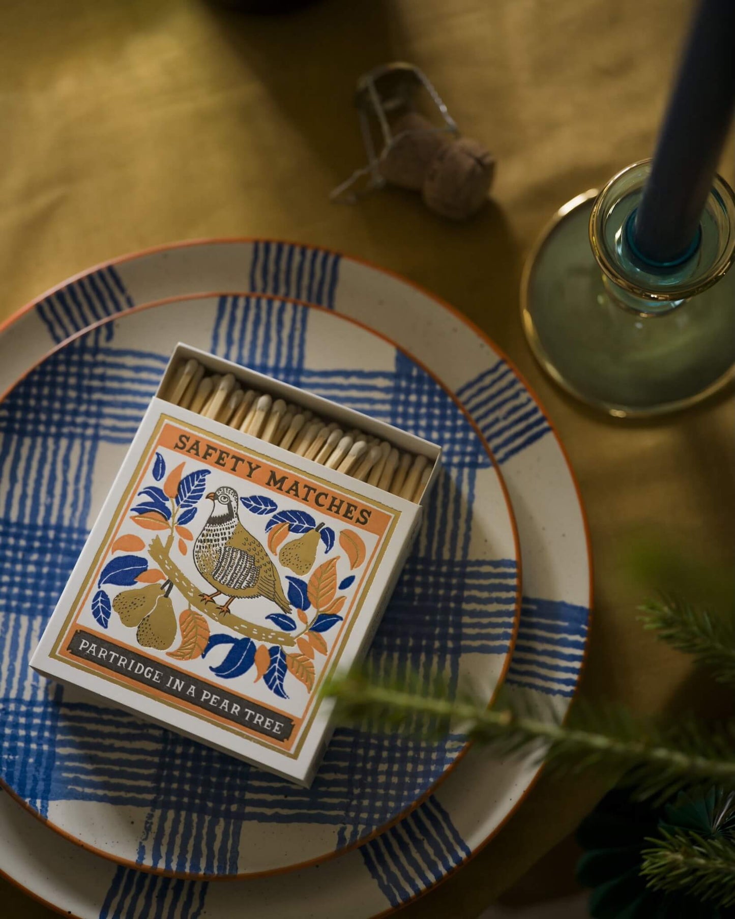 Matches box with decorative design on a table with a candle and checked plates.