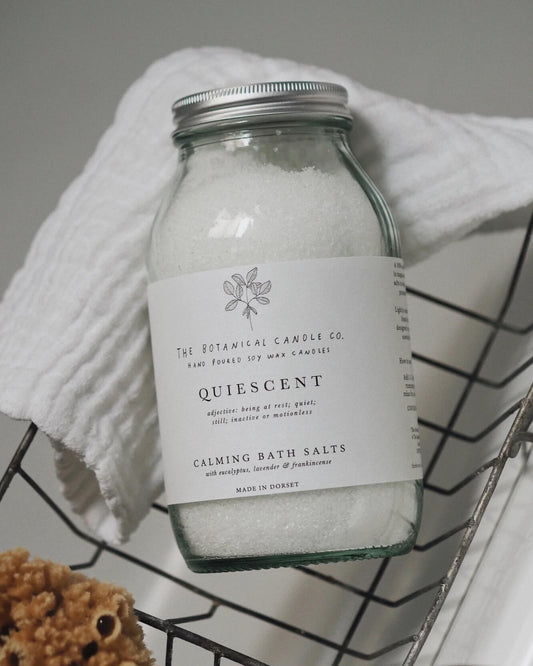 Bottle of 'Quiescent' calming bath salts from The Botanical Candle Co. on a wire rack.