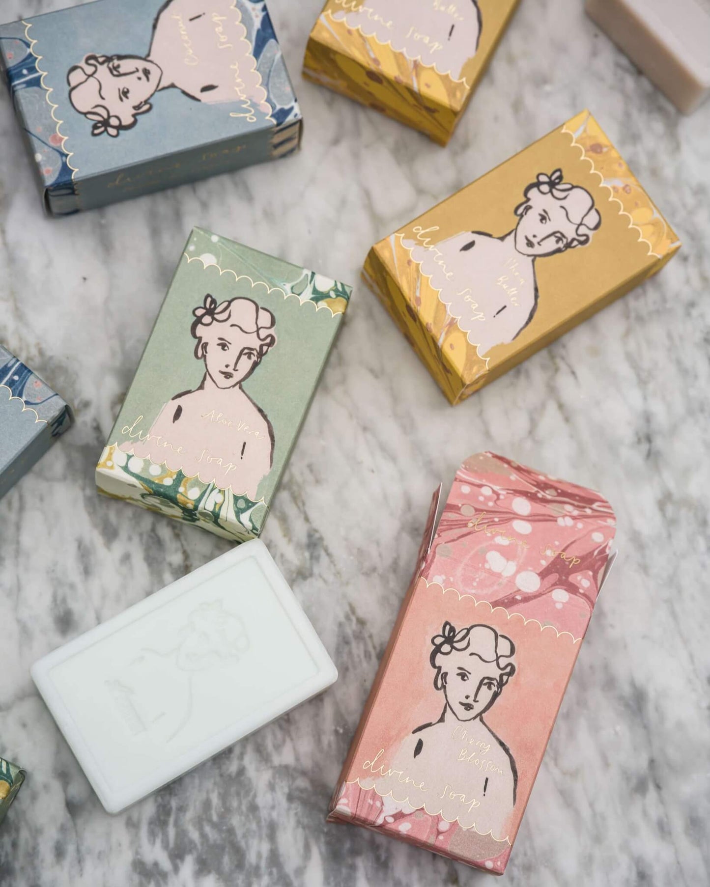 Soap bars with decorative boxes featuring illustrations of women on a marble surface