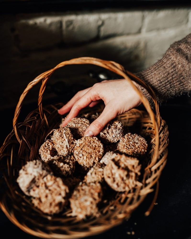 Hand reaching into a woven basket filled with firelighters against a stone wall background.