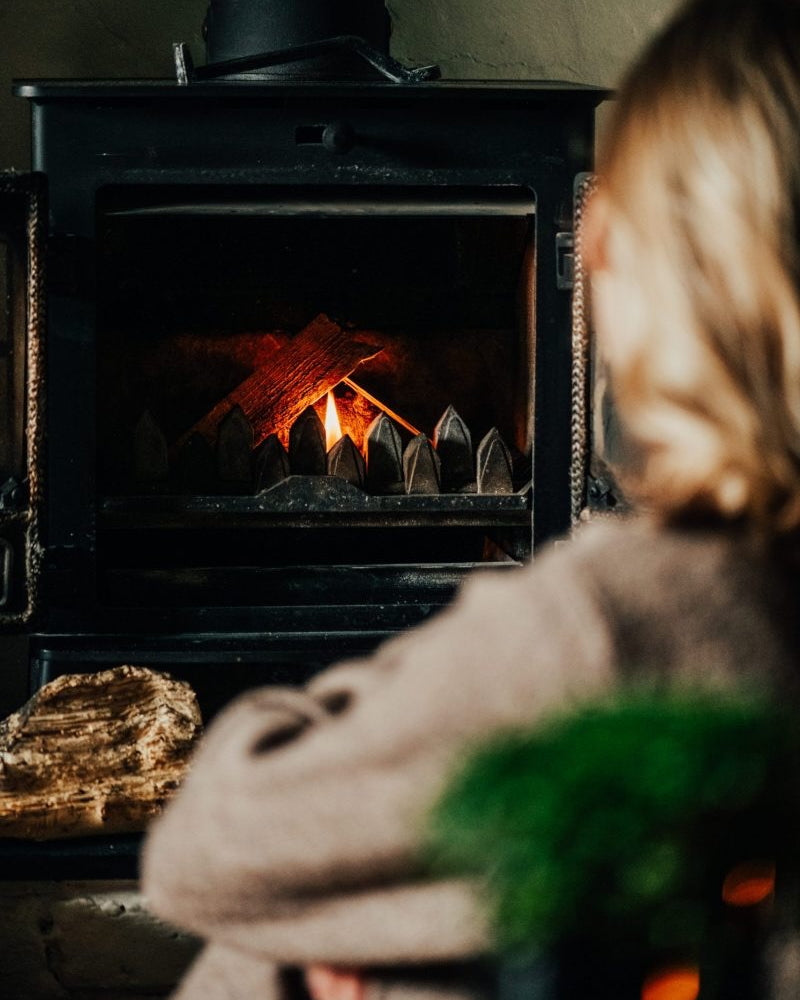 Person sitting in front of a wood stove with a fire burning inside