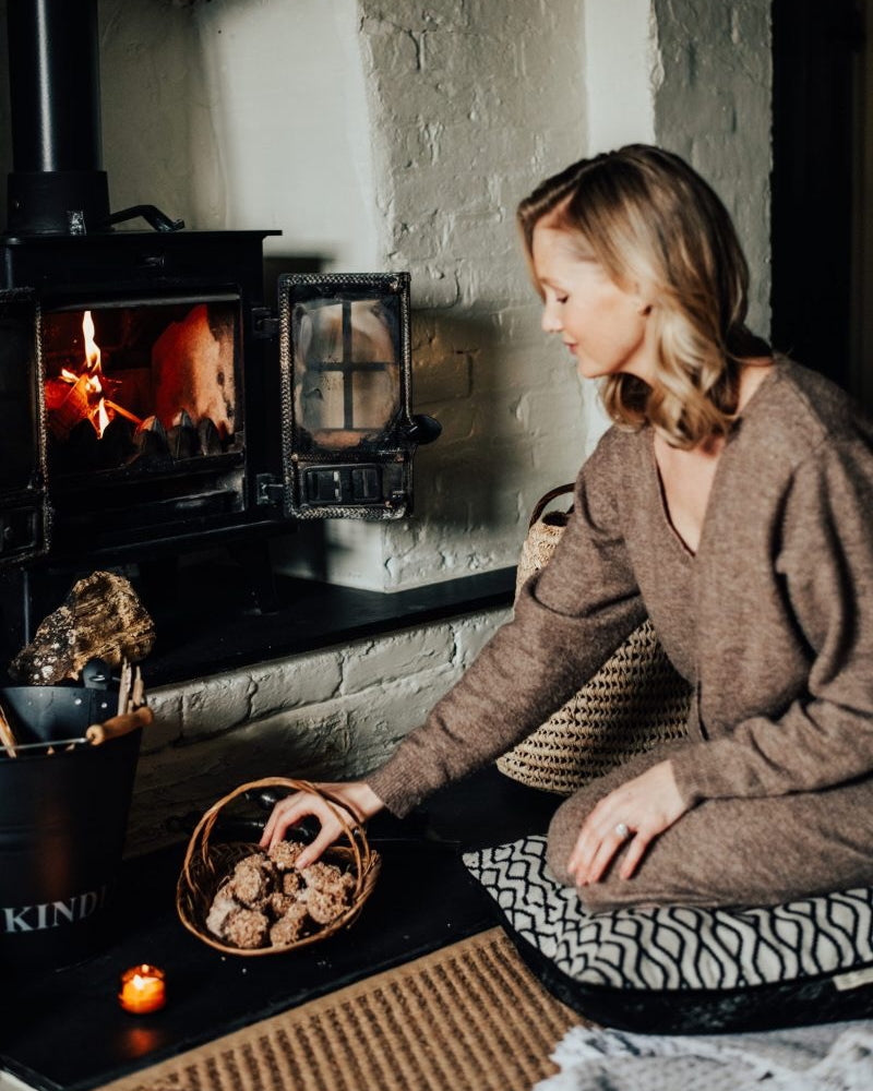Woman sitting by a fireplace with a basket of firelighters.