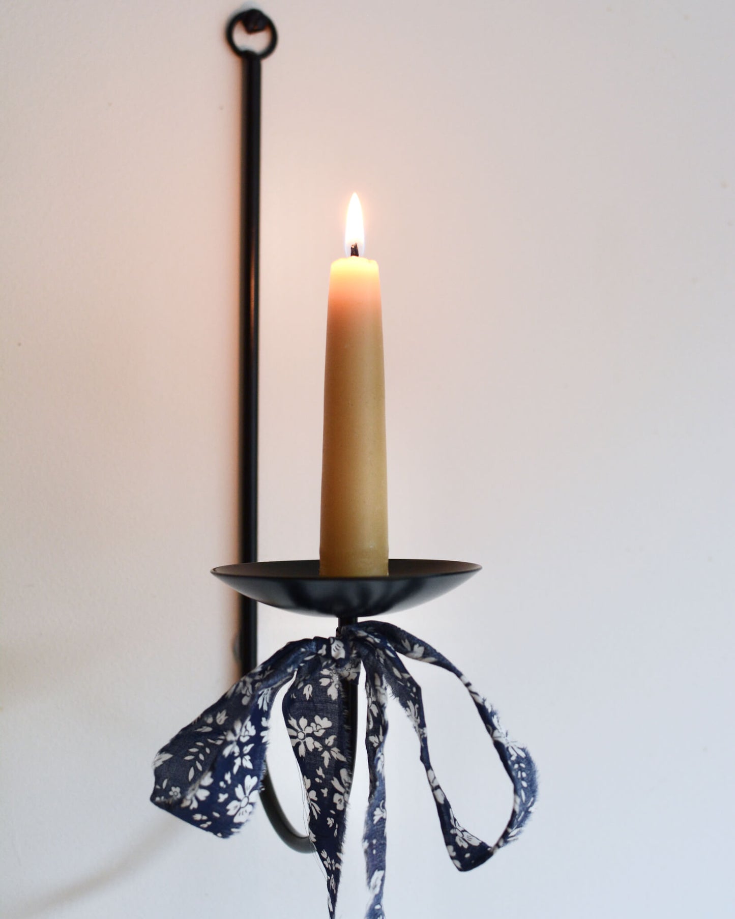 A close-up of a single black metal wall sconce candle holder with a lit beeswax stubby candle.
