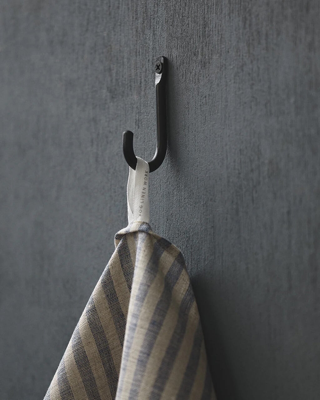 Black iron wall hook with a striped towel on a grey wall