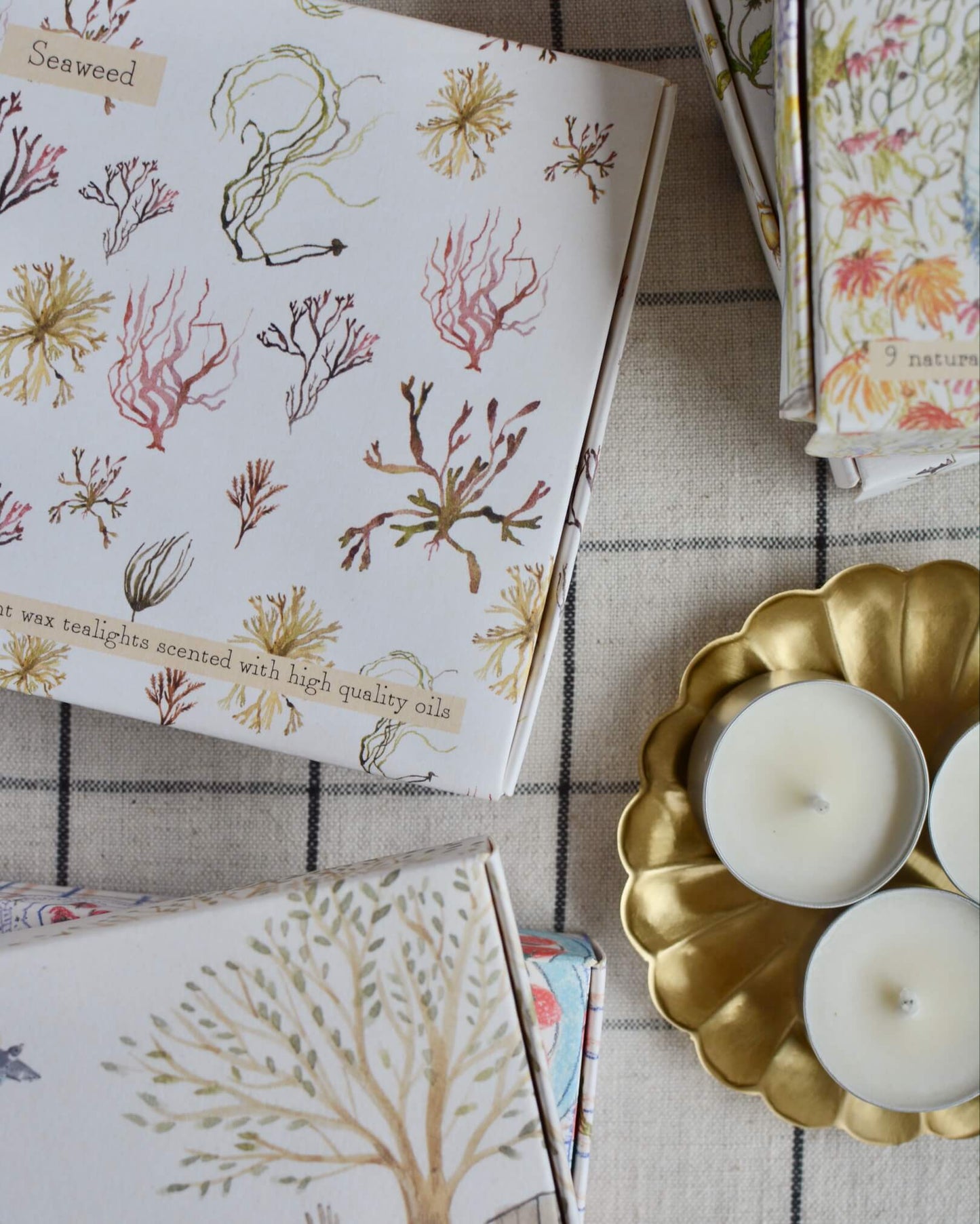 A collection of illustrated boxes of tealights, alongside a brass tea light dish.