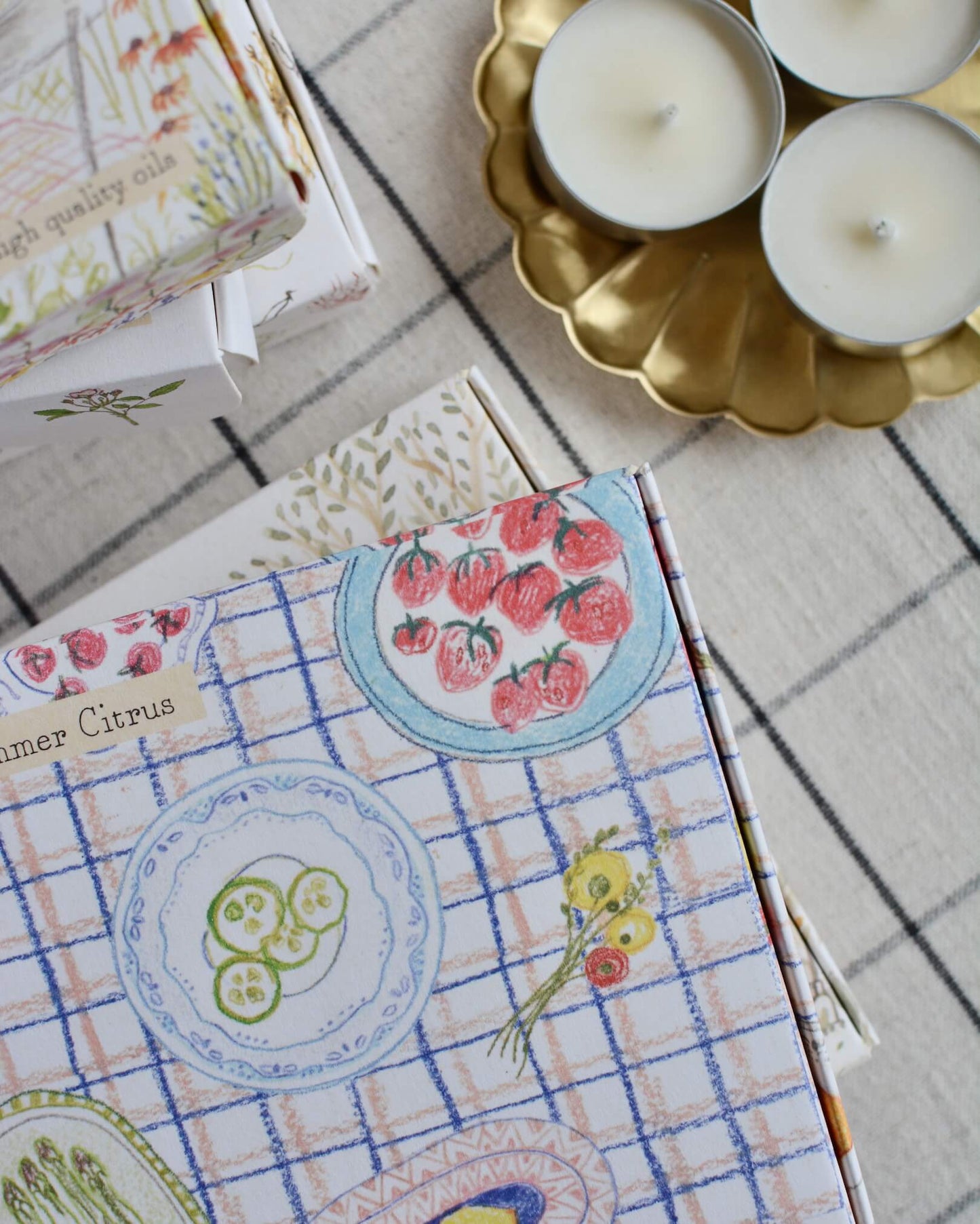 Illustrated boxes of tea lights, next to a brass floral-shaped candle dish.