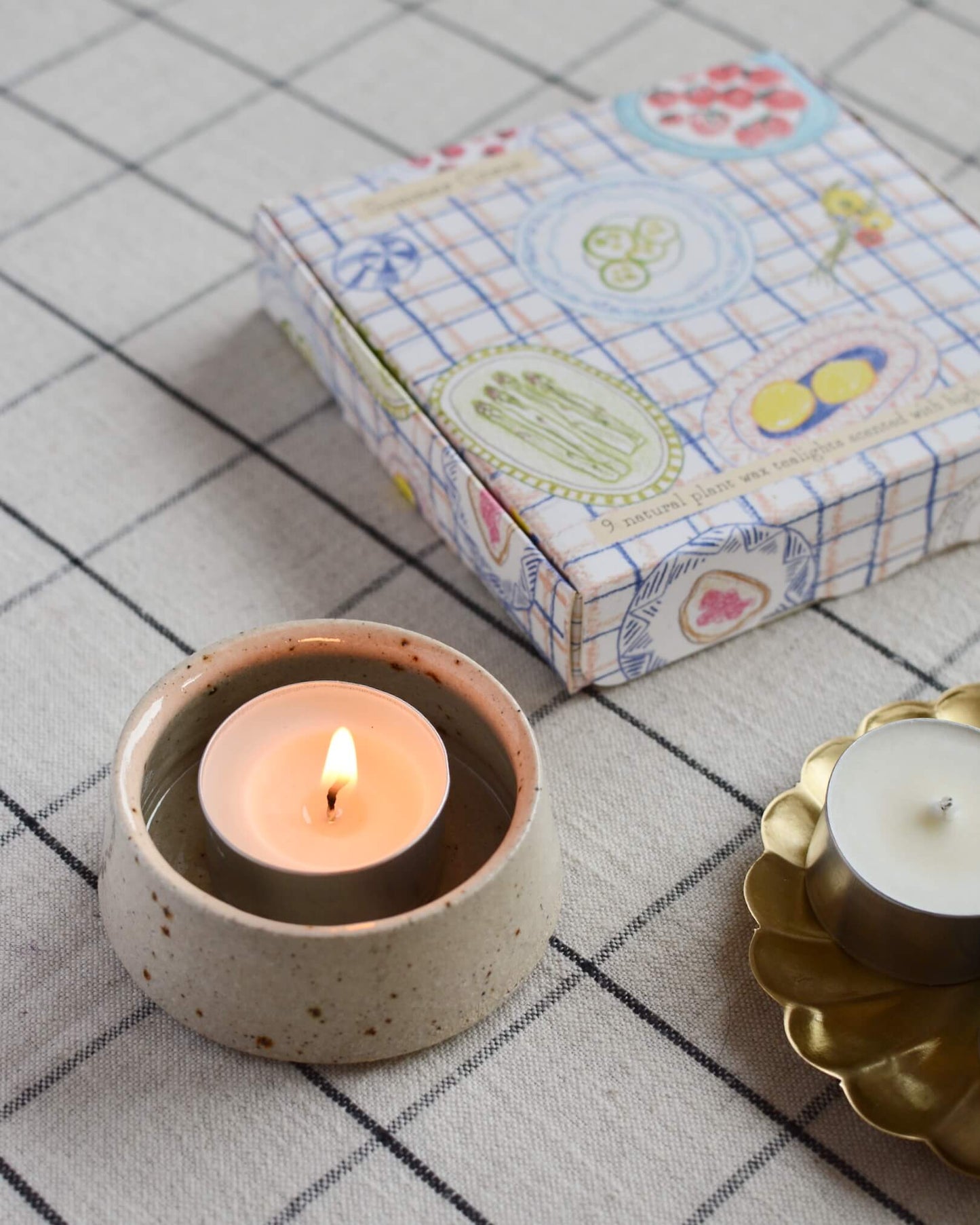 A lit tea light, within a ceramic holder.