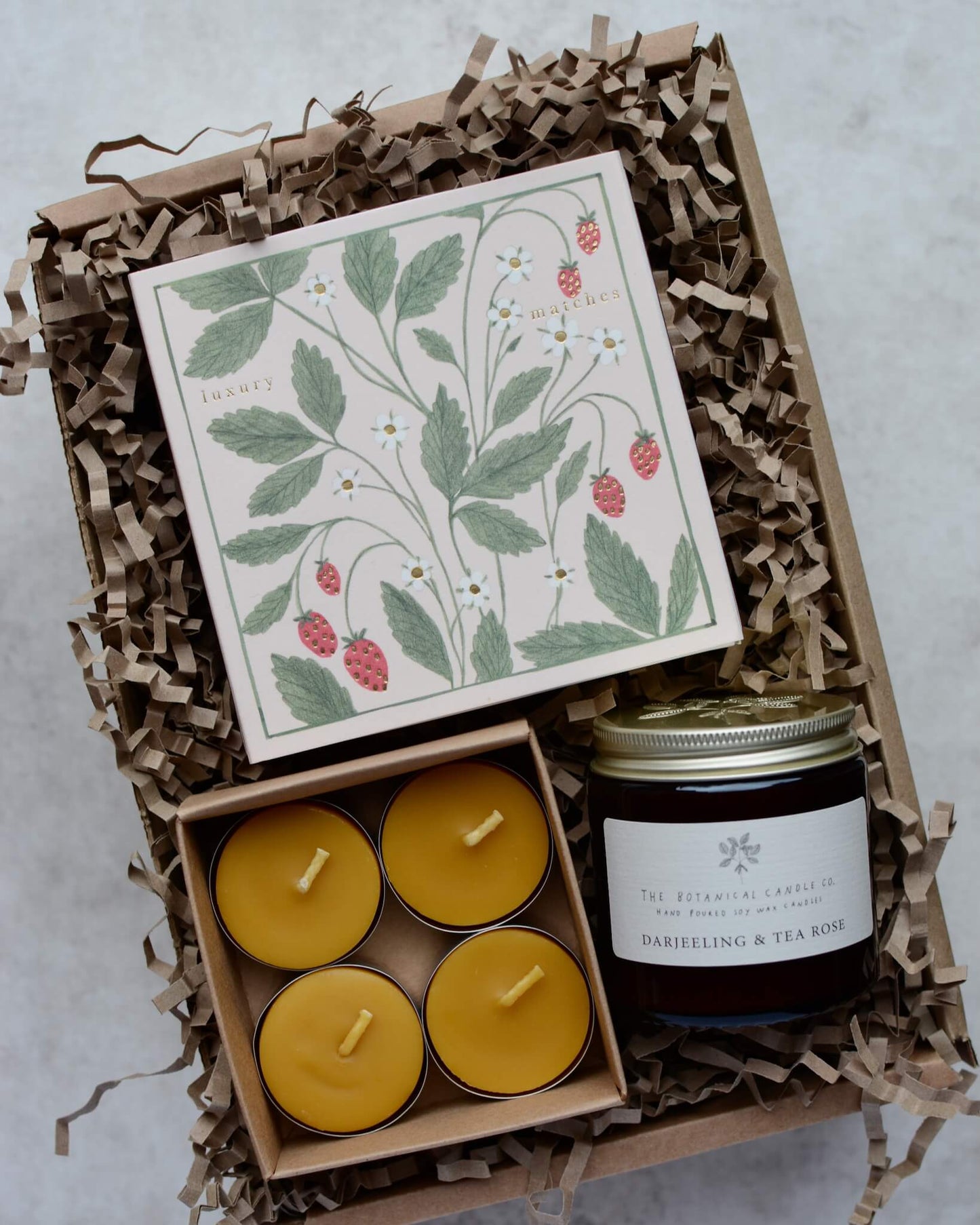 A candle gift box containing a scented rose candles, 4 beeswax tea lights and a box of strawberry-design matches.