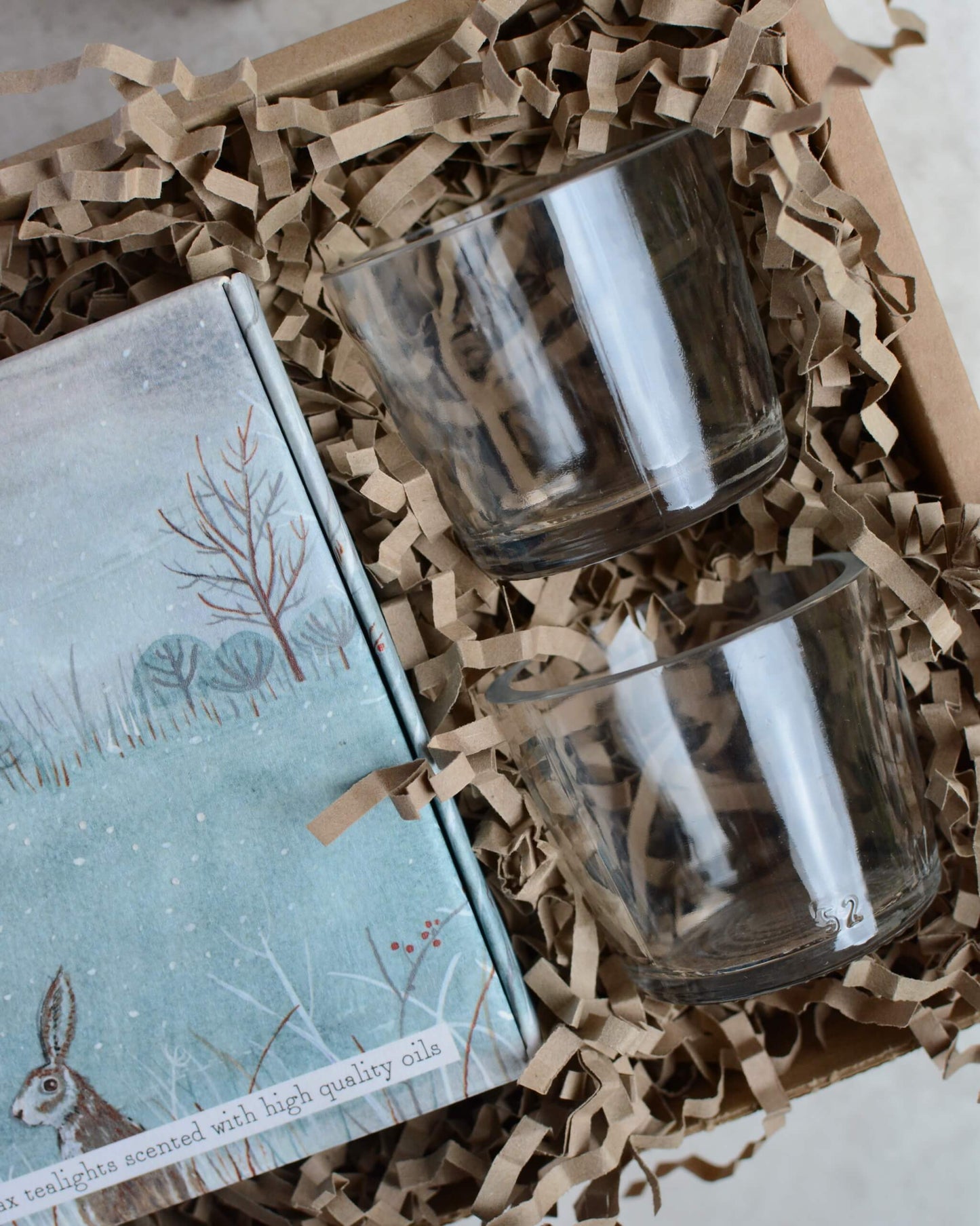 Gift set with a box of tealights and a pair of glass votives, in a box on a grey surface.
