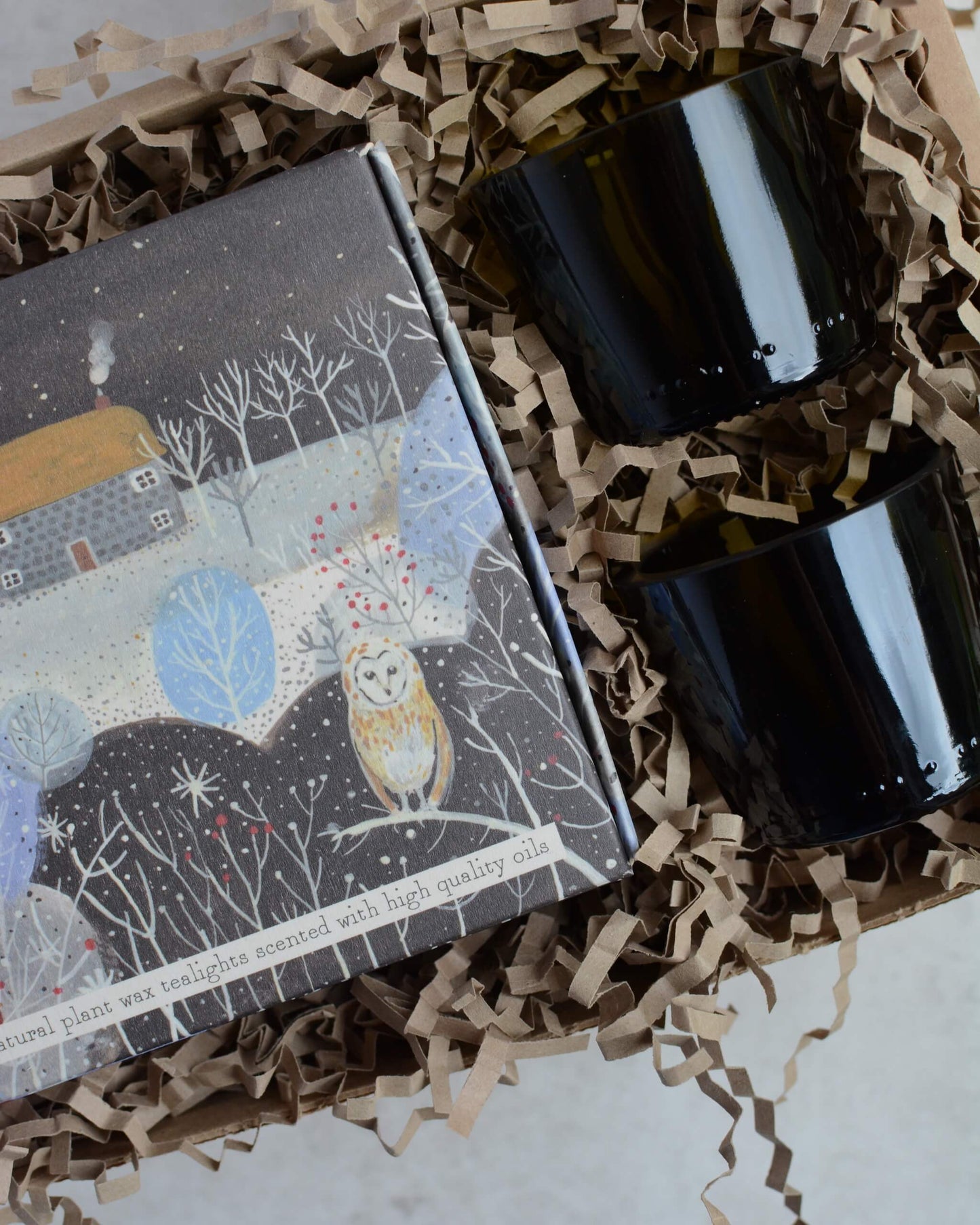 Two lit candles in glass votives, next to a box of illustrated tealights.