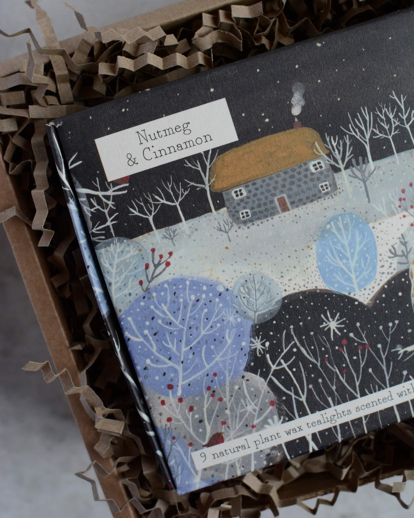 A box of tealights with a winter scene design and 'Nutmeg & Cinnamon' text.