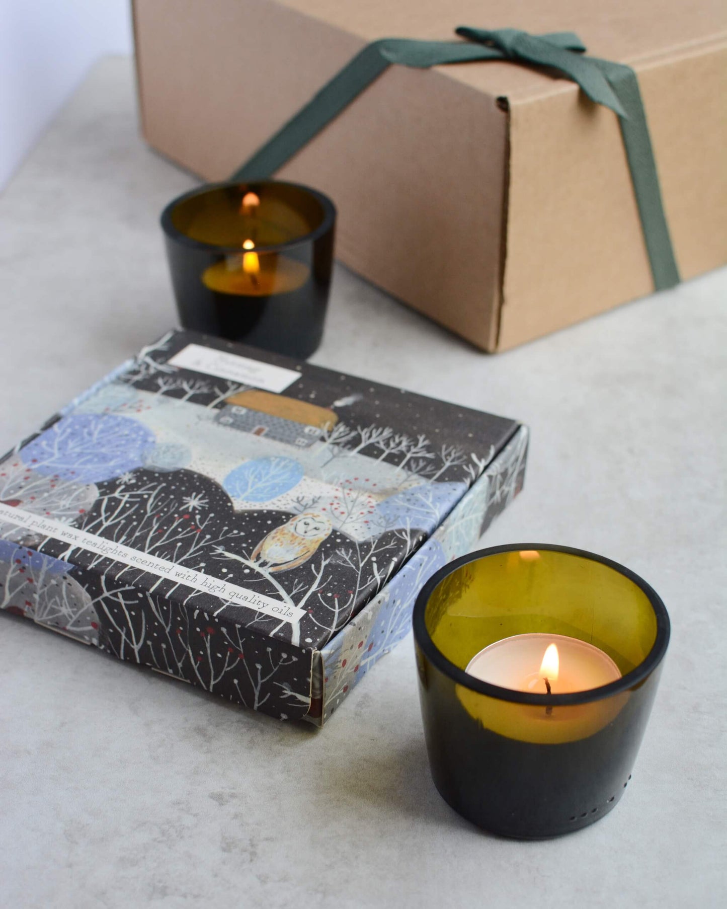 Two lit candles in glass votives, next to a box of illustrated tealights.