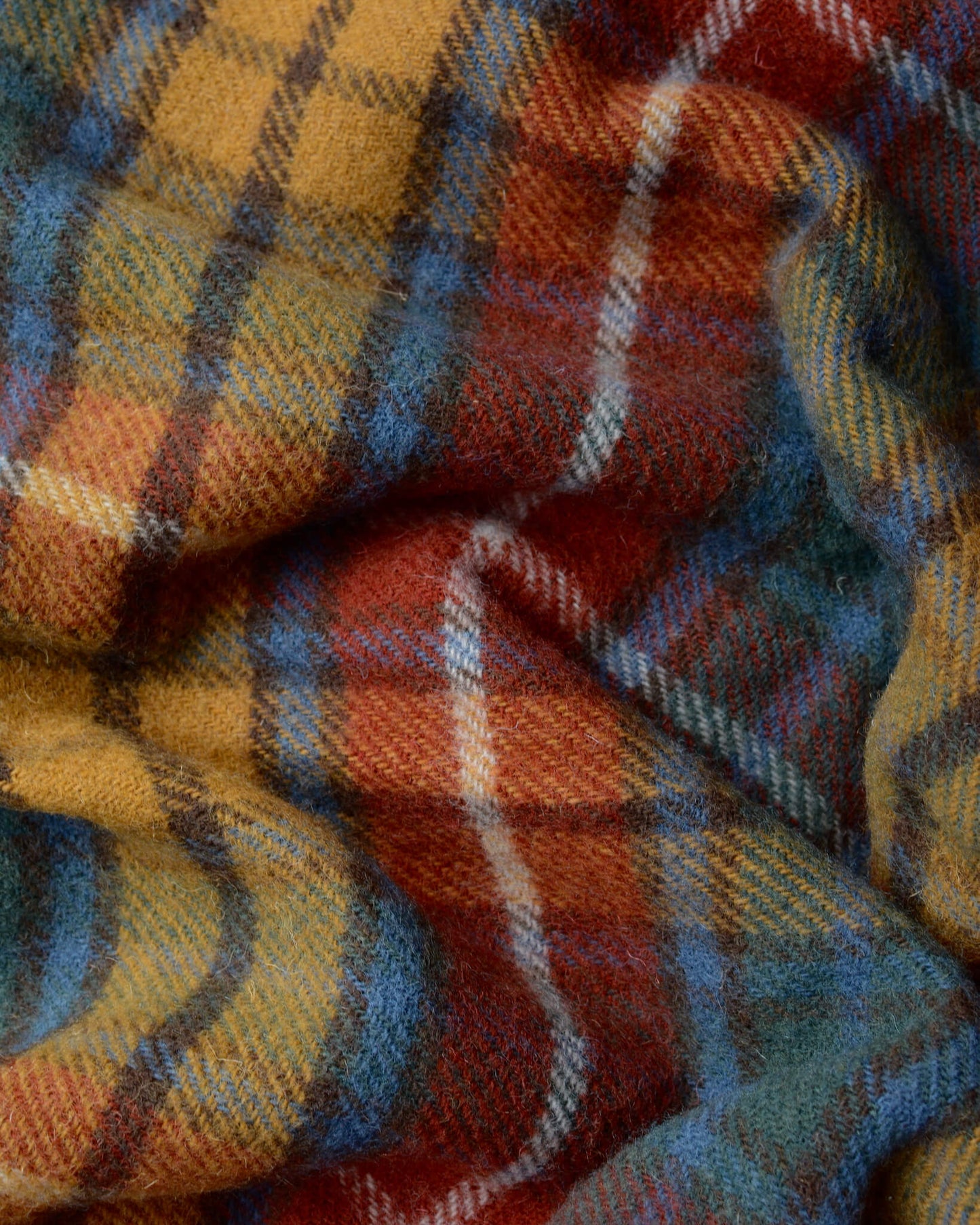 Close up of a plaid wool blanket, with tones of red, yellow and blue.