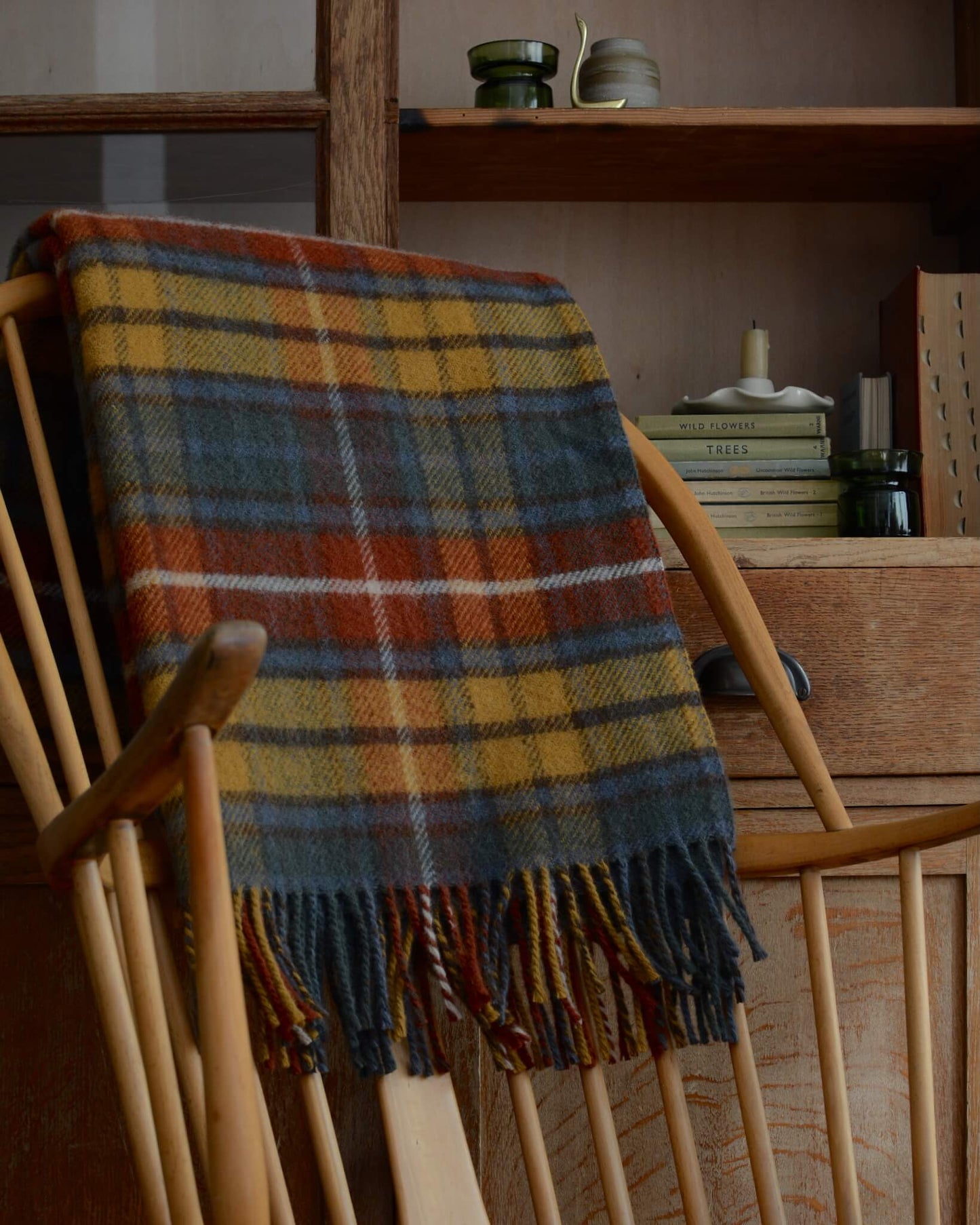 A plaid wool blanket, with tones of red, yellow and blue, shown on a wooden rocking chair.