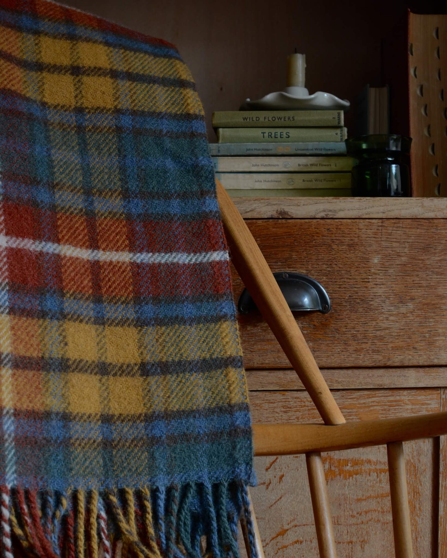 A plaid wool blanket, with tones of red, yellow and blue, shown on a wooden rocking chair.