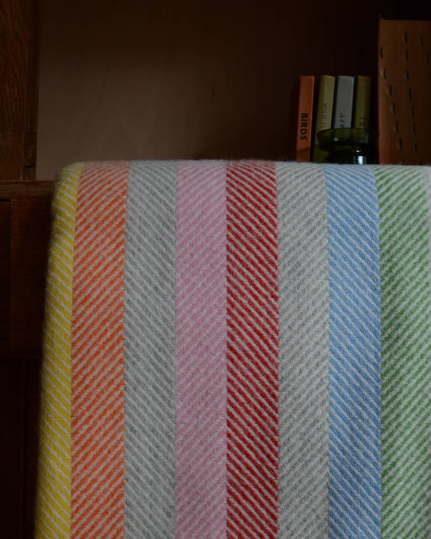 Close up of a colourful rainbow striped wool blanket with books shown behind.