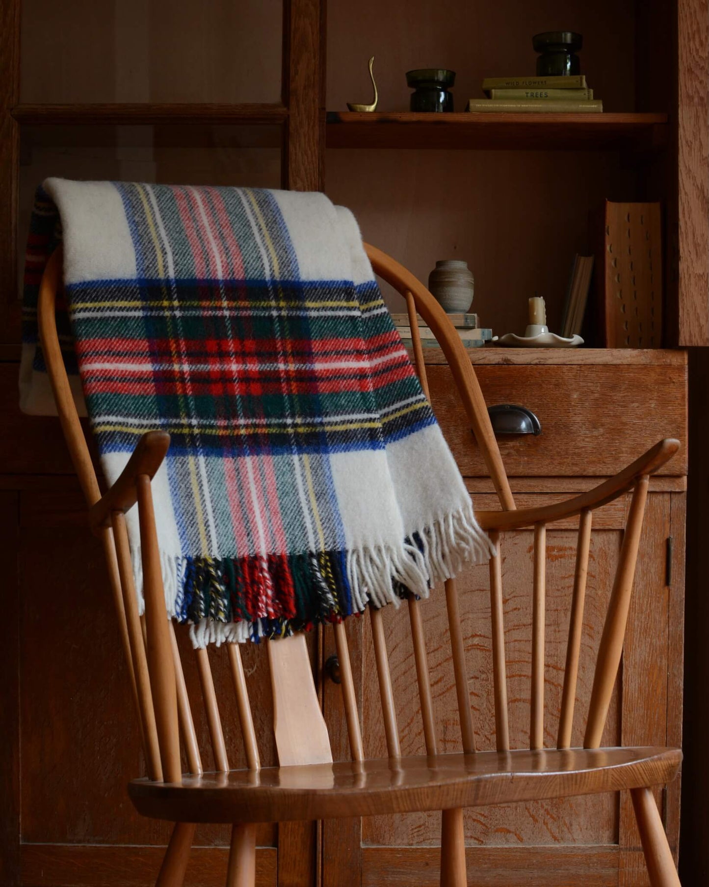 Plaid wool blanket with colourful pattern, shown on a wooden rocking chair.