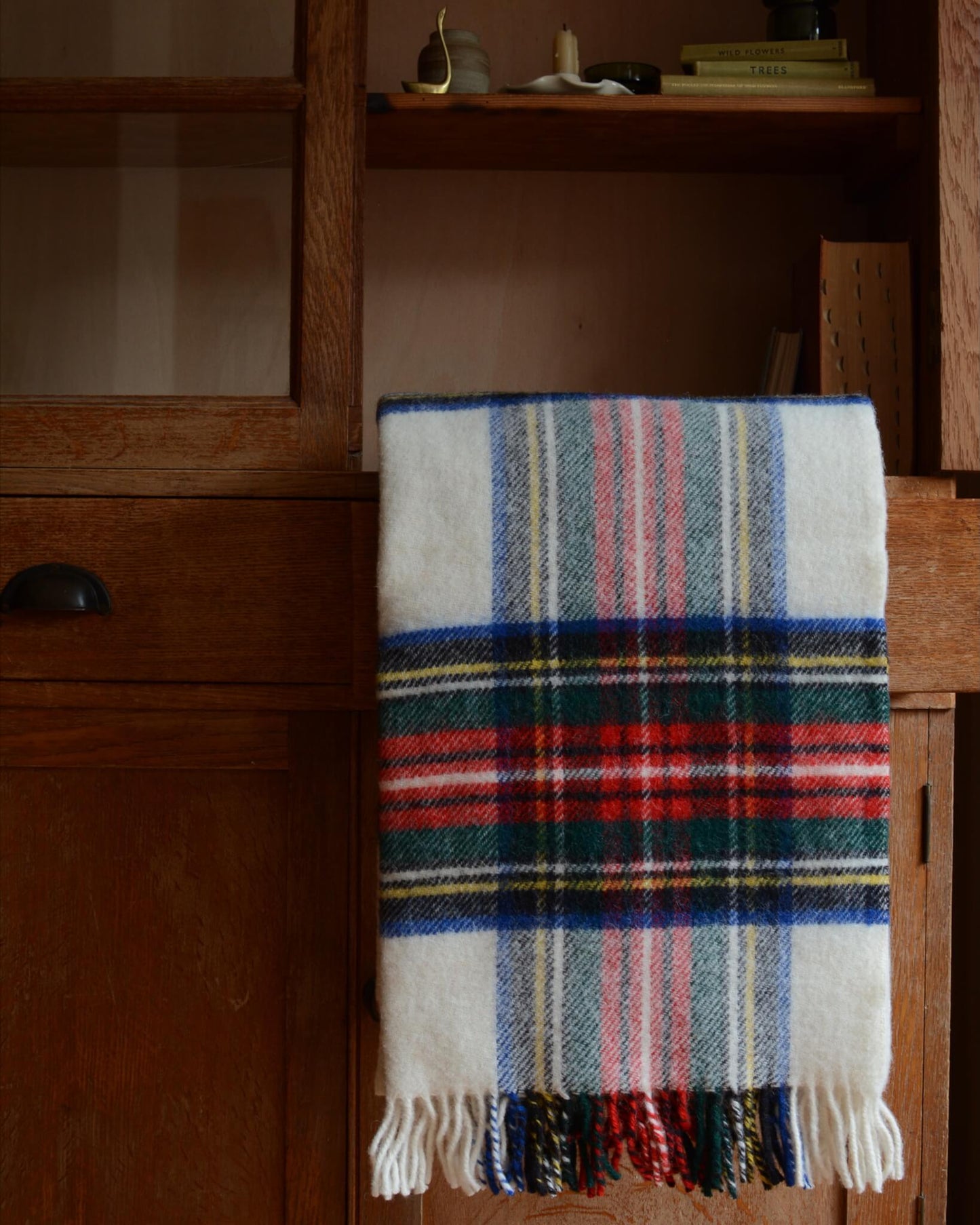 Plaid wool blanket with colourful pattern, shown on a wooden cabinet.