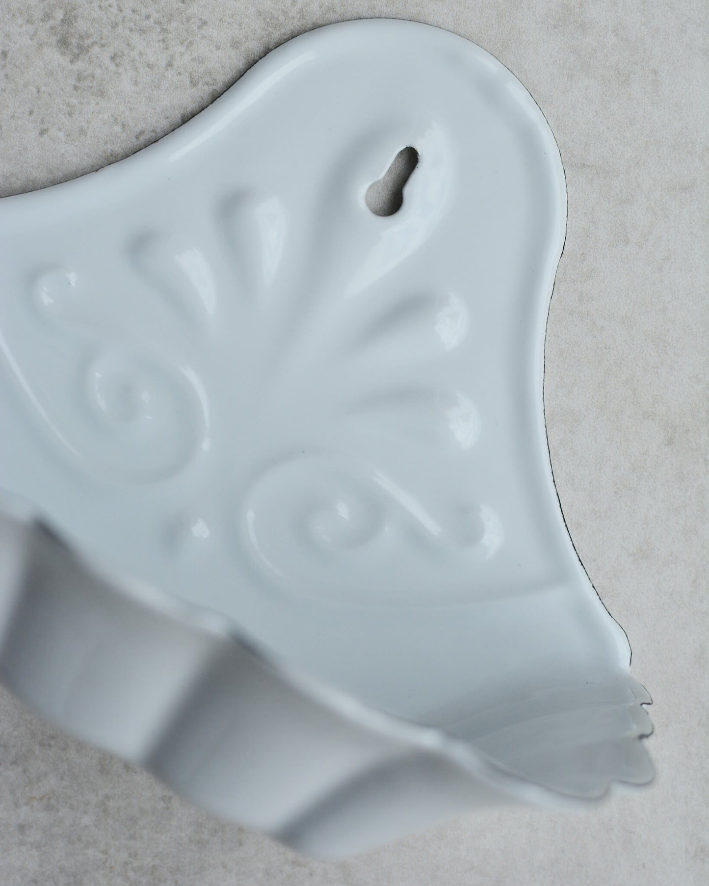Vintage-style white enamel wall-mounted soap dish, with floral pattern, on a grey background.