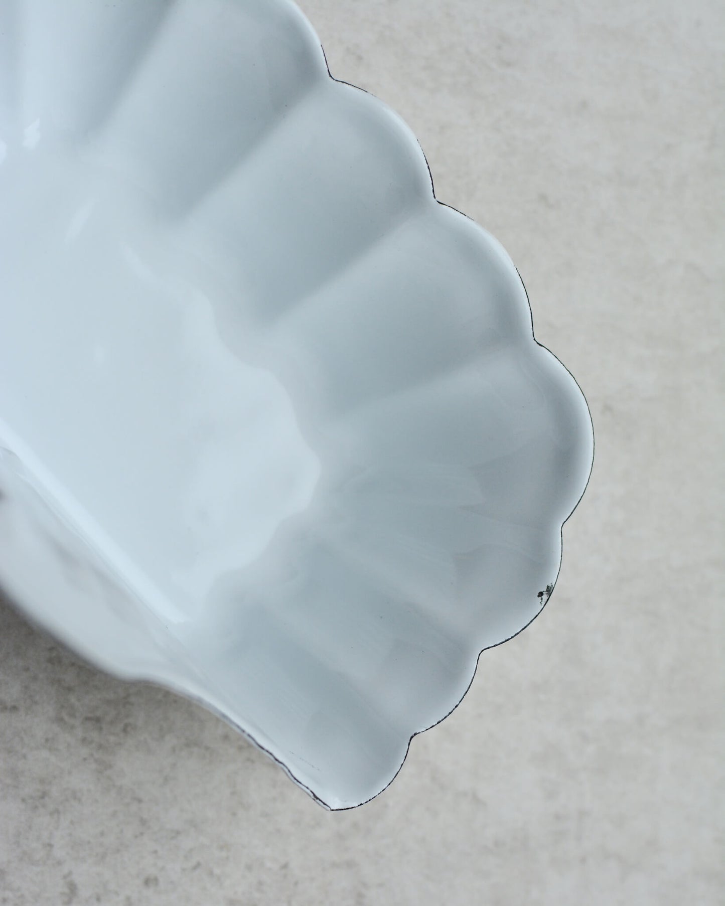 Close-up of a white enamel wall-mounted soap dish, with floral pattern, on a grey background.